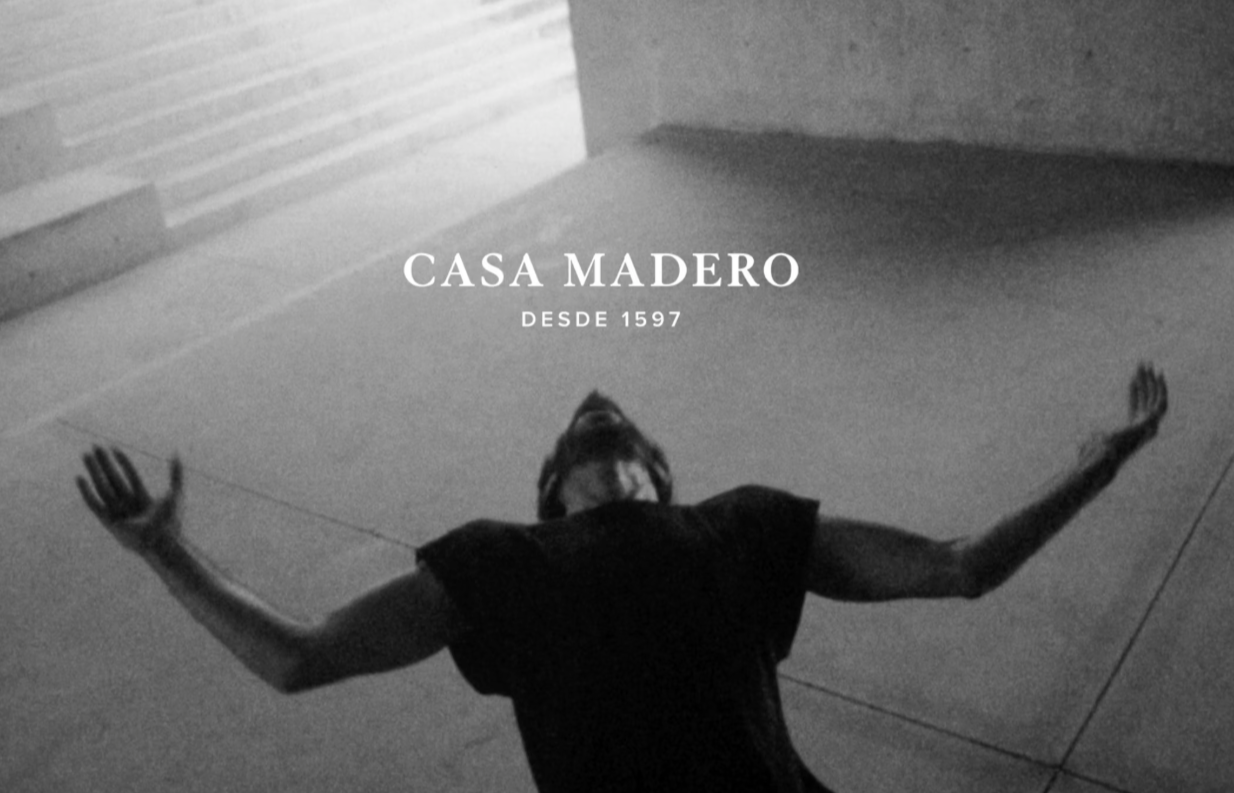 Black and white photo of a person lying on the ground with arms outstretched, with text overlay: "Casa Madero Desde 1597".