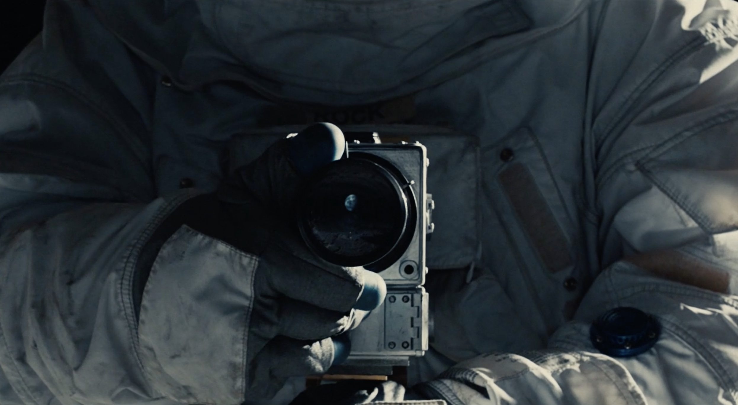 Close-up of astronaut in space suit holding a vintage camera, with Earth visible through the camera's lens.