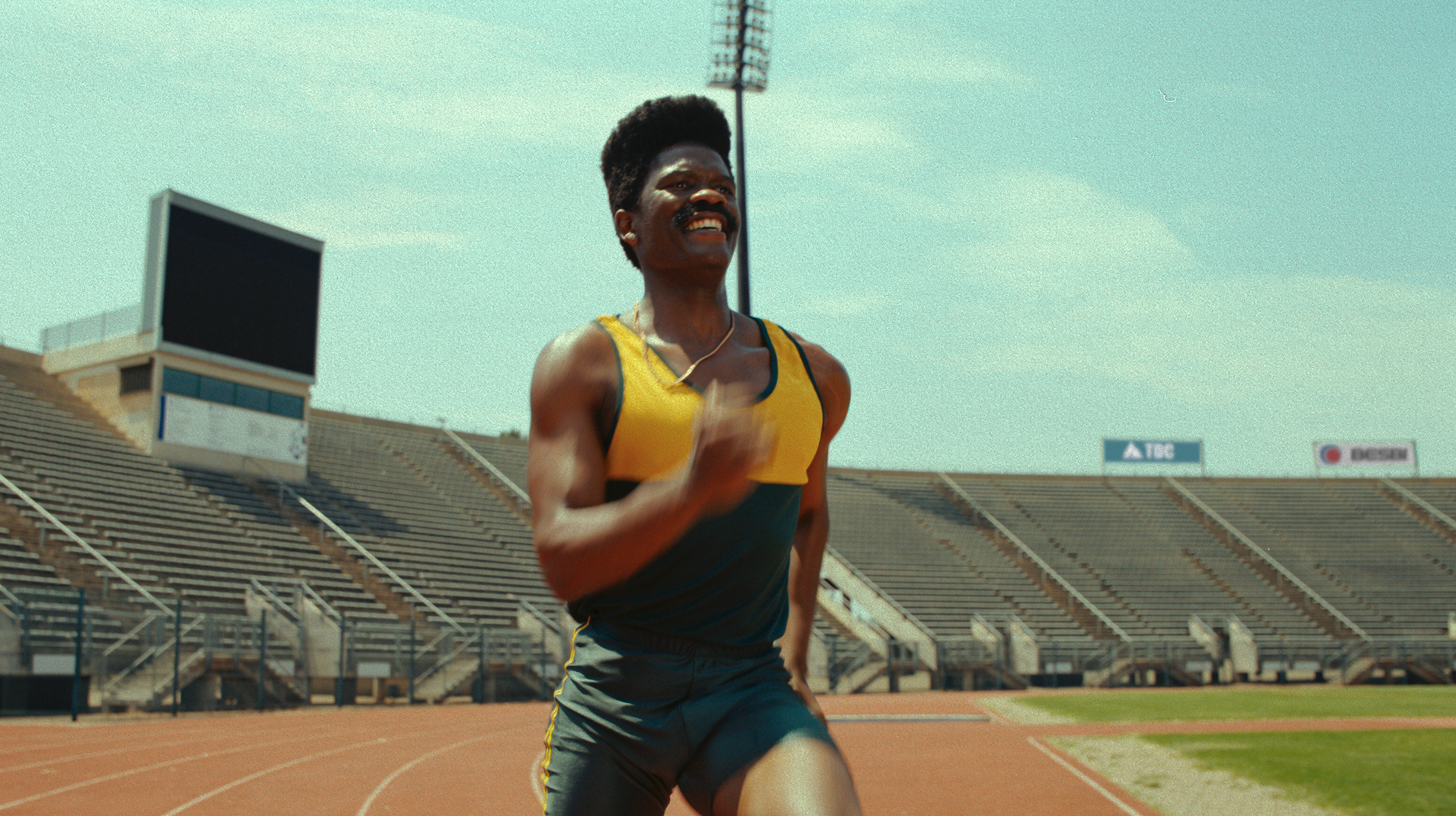 A male athlete in a yellow and black sports uniform running on a track in a stadium.