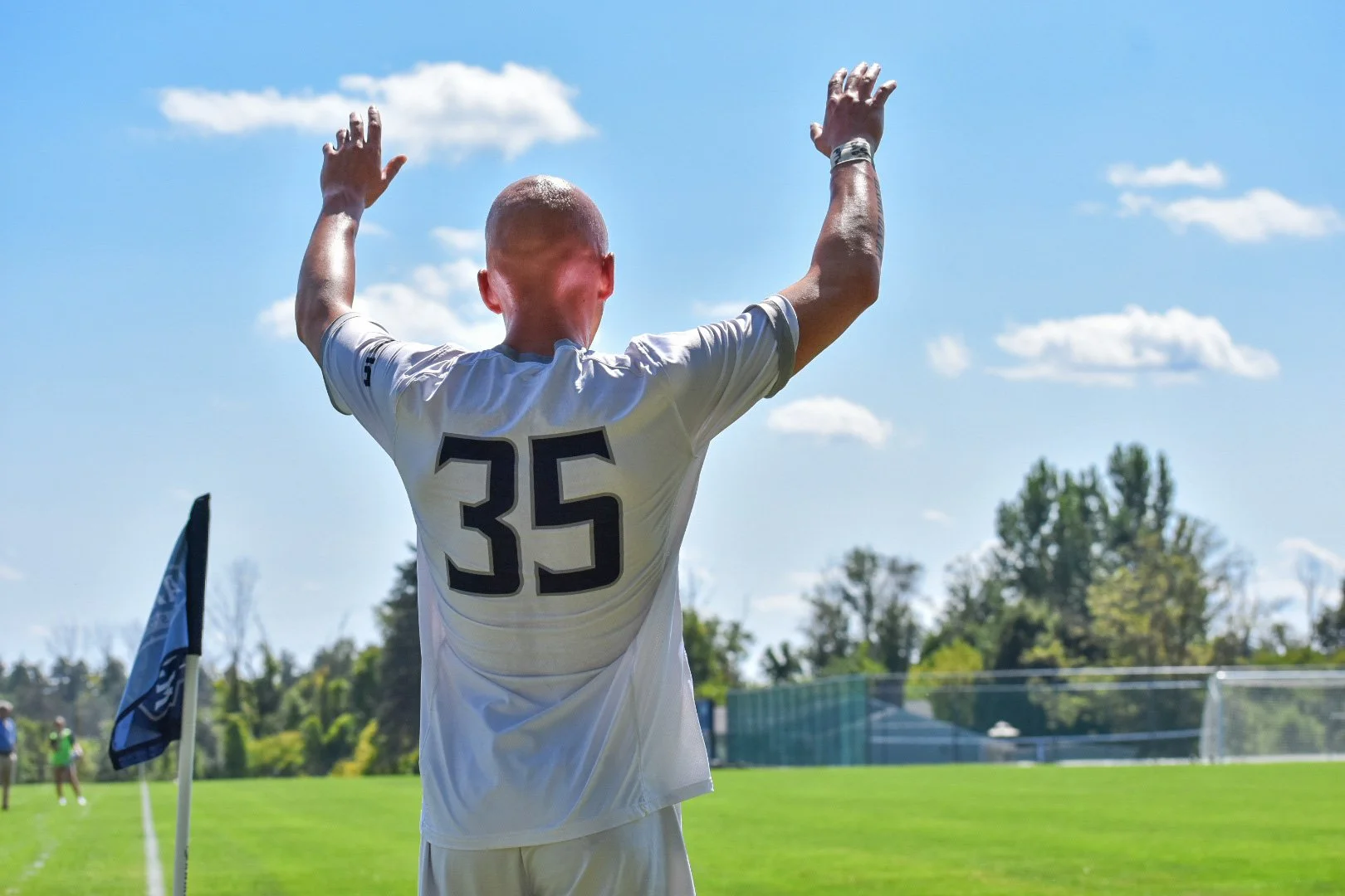 A soccer player wearing a white jersey with the number 35, raising his hands in celebration on a sunny soccer field.