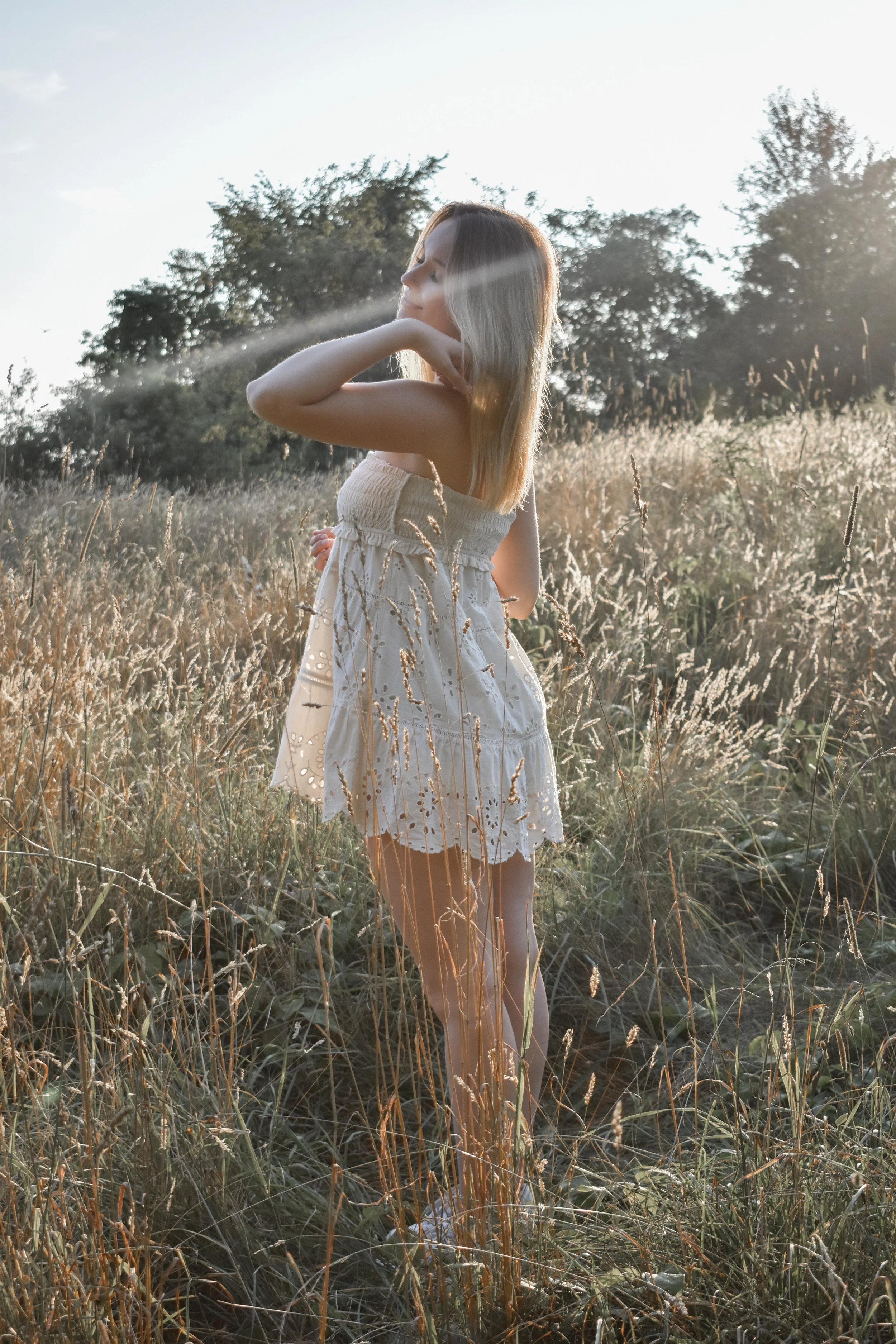 A woman in a white dress standing in a field of tall grass during sunset.