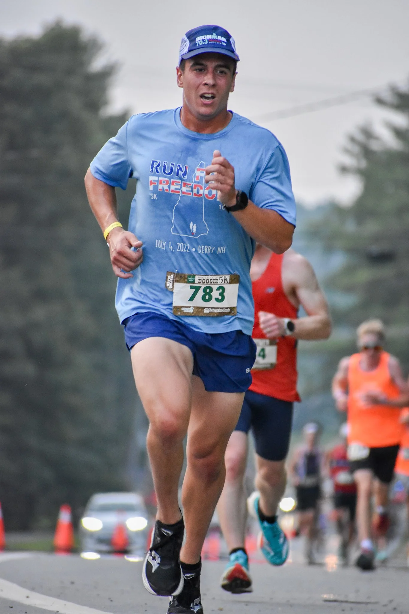A young man running in a marathon, wearing a light blue T-shirt with the words 'Run for Freedom', a blue cap, and shorts, with a race bib numbered 783.
