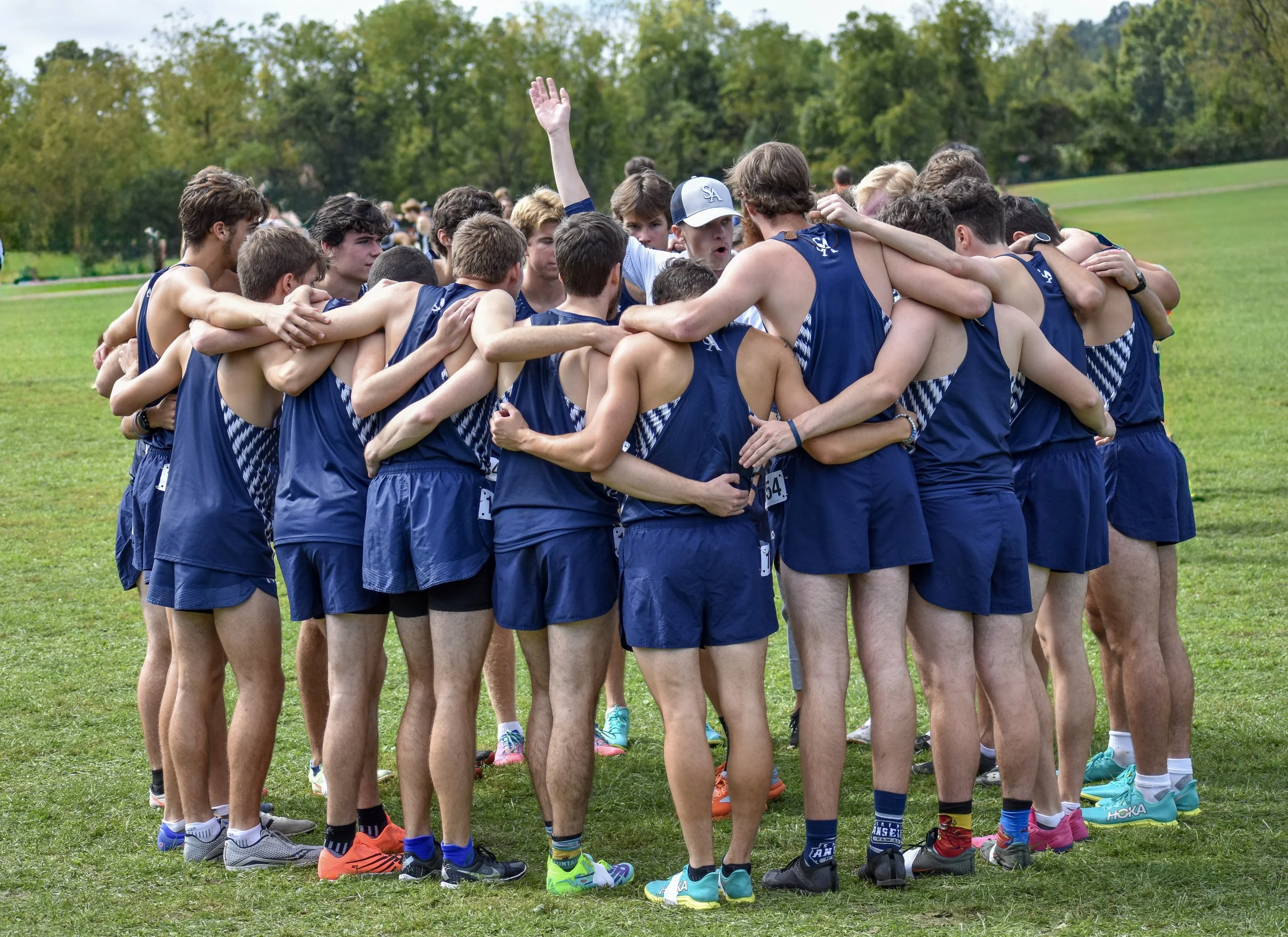 A group of young male athletes huddled together on a grassy field, wearing matching blue athletic uniforms, likely preparing for a race or team event.