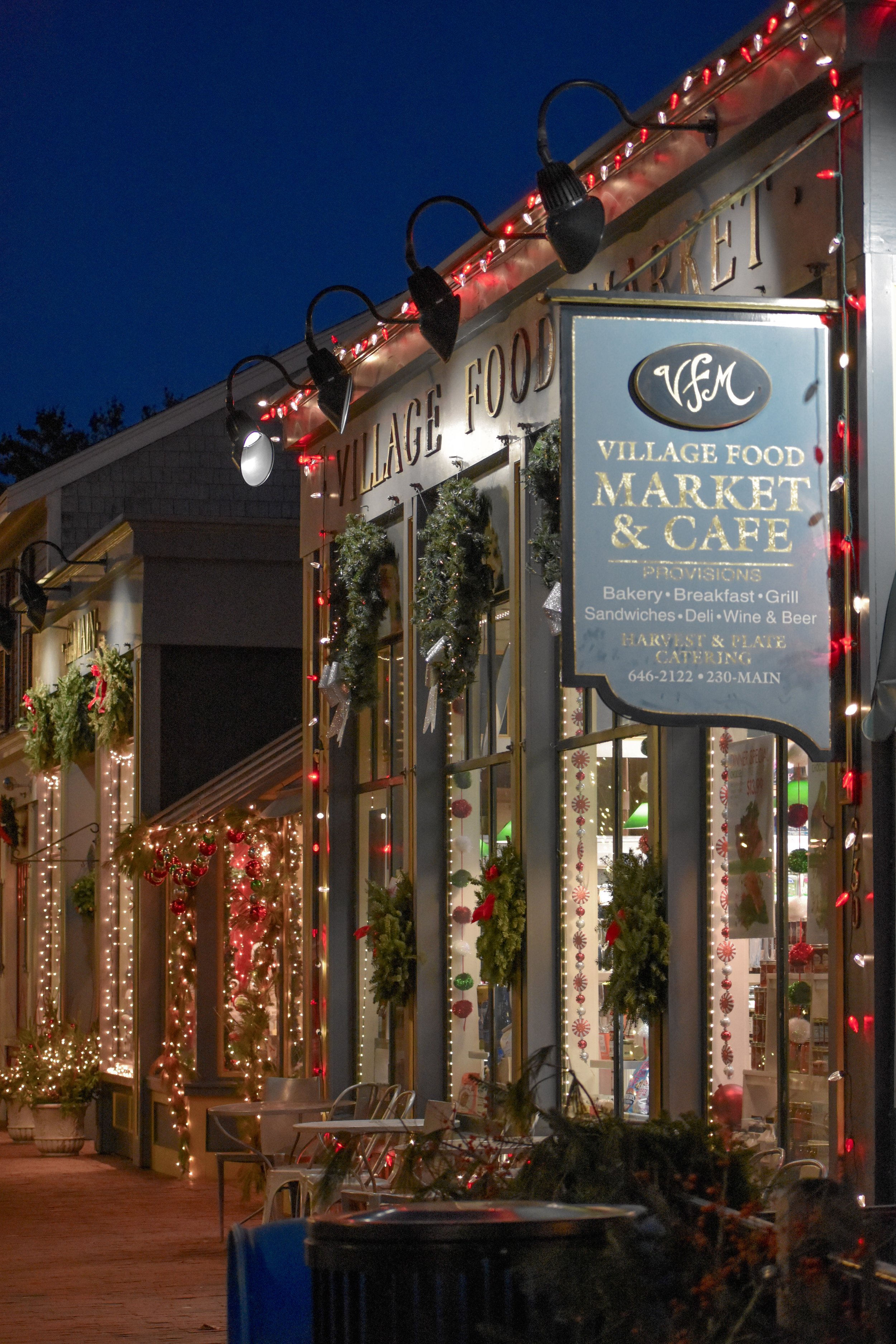 Exterior of Village Food Market & Cafe decorated with Christmas lights and wreaths during evening.