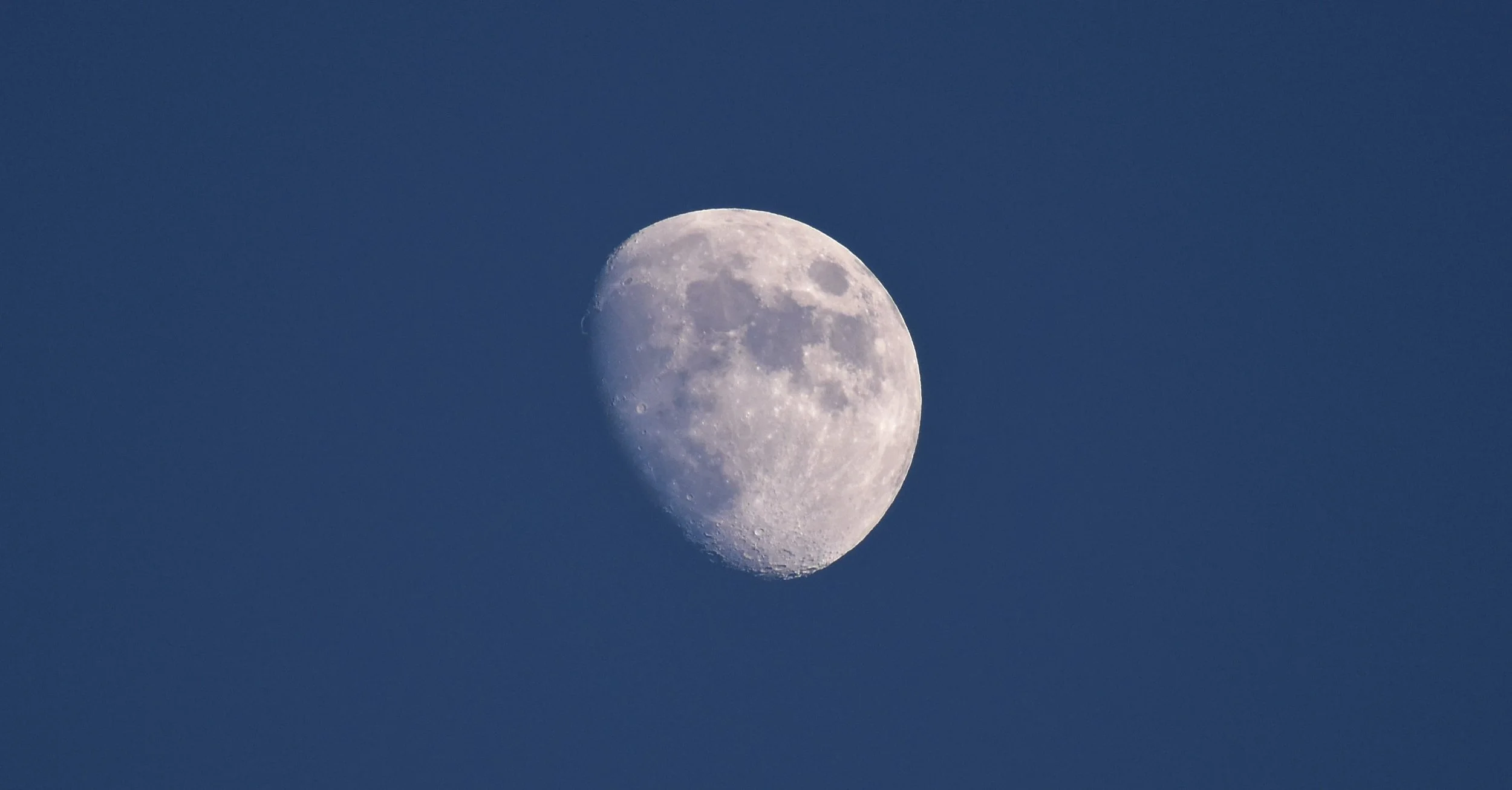 A clear photograph of the moon in a waxing gibbous phase against a dark blue sky.