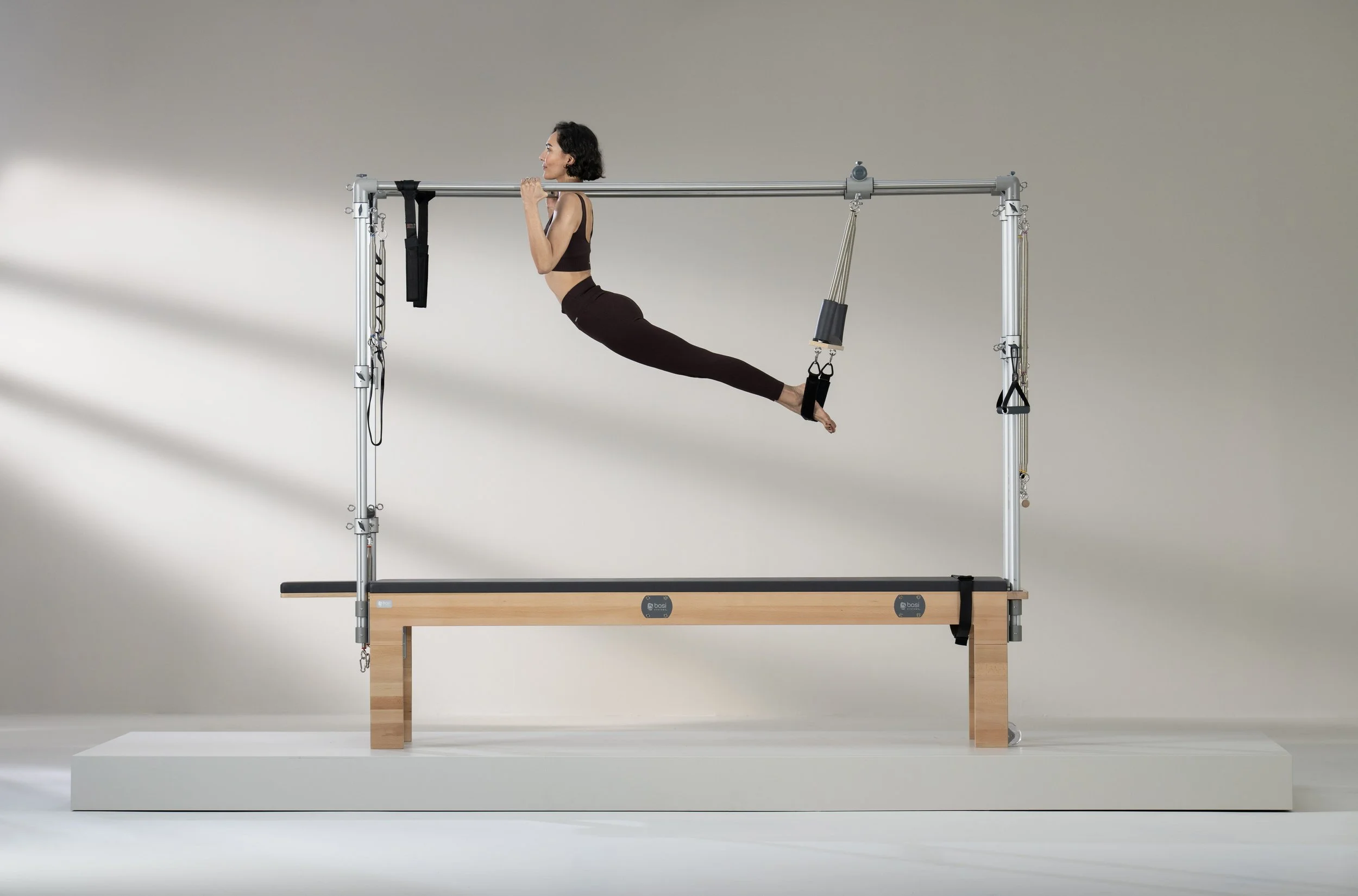 Een vrouw die Pilates op een reformer apparaat doet, in een kamertje met een neutrale achtergrond.