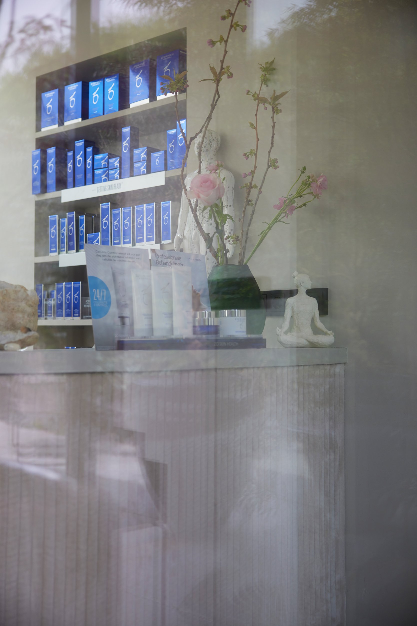 Een winkelinterieur met blauwe producten op planken, een vaas met takken en bloemen, en twee witte decoratieve beelden in meditatiepositie.