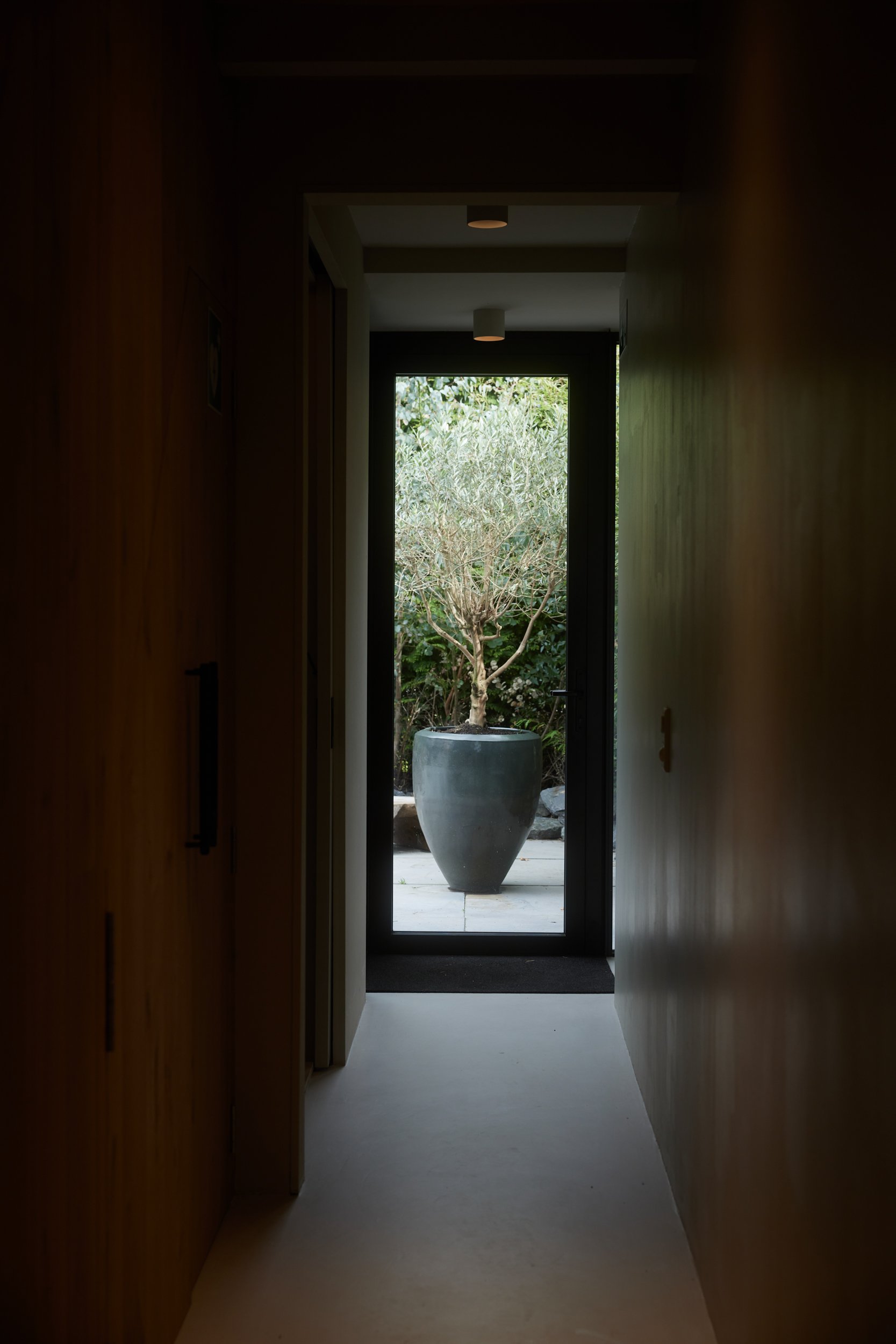 Doorgang met uitzicht op een tuin met een grote pot en een boom.