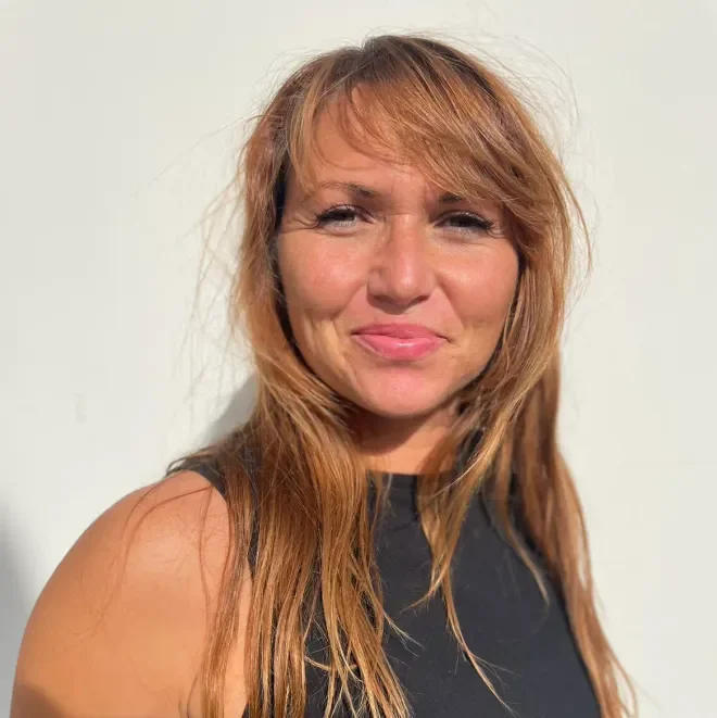 A woman with red hair, wearing a black sleeveless top, smiling softly against a plain white background.