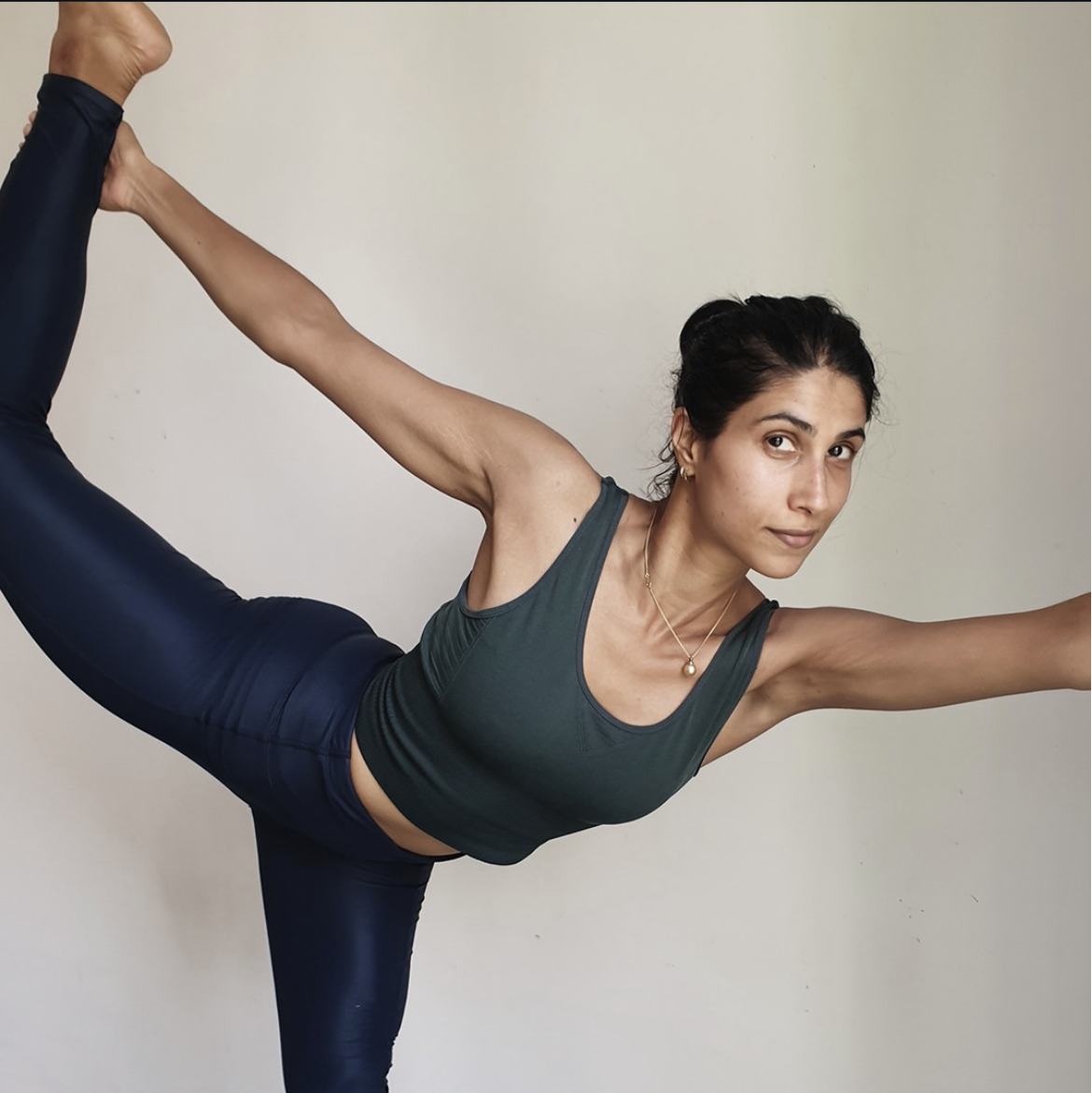 Woman in athletic wear performing a yoga pose against a plain wall.