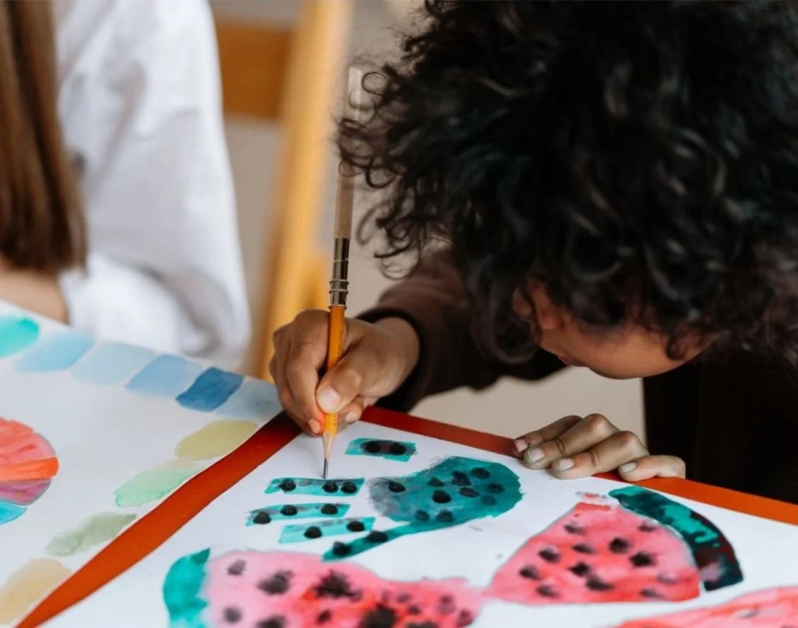 Person painting colorful, abstract shapes with black dots on a piece of paper.
