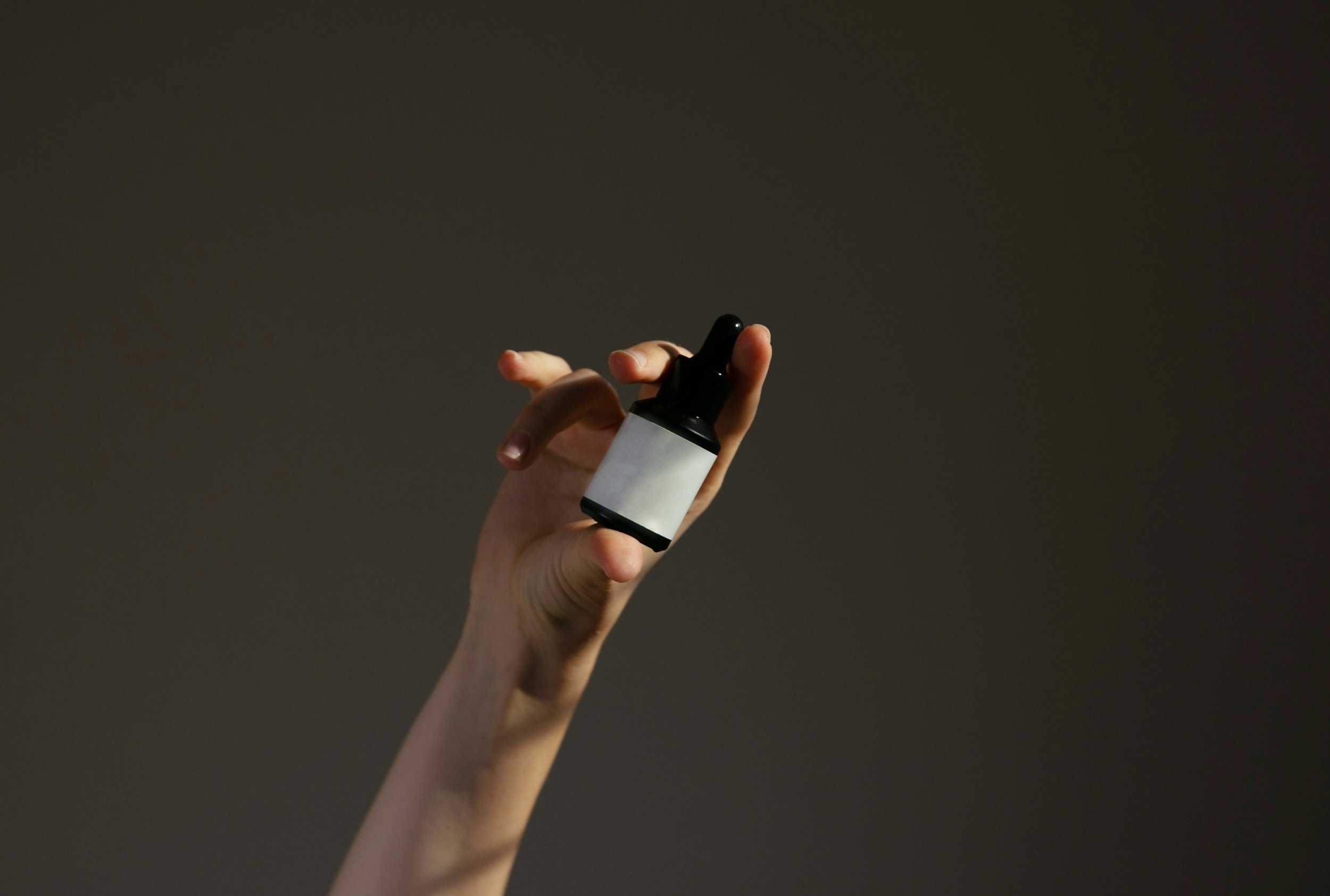 A hand holding a small black and white dropper bottle against a dark background.