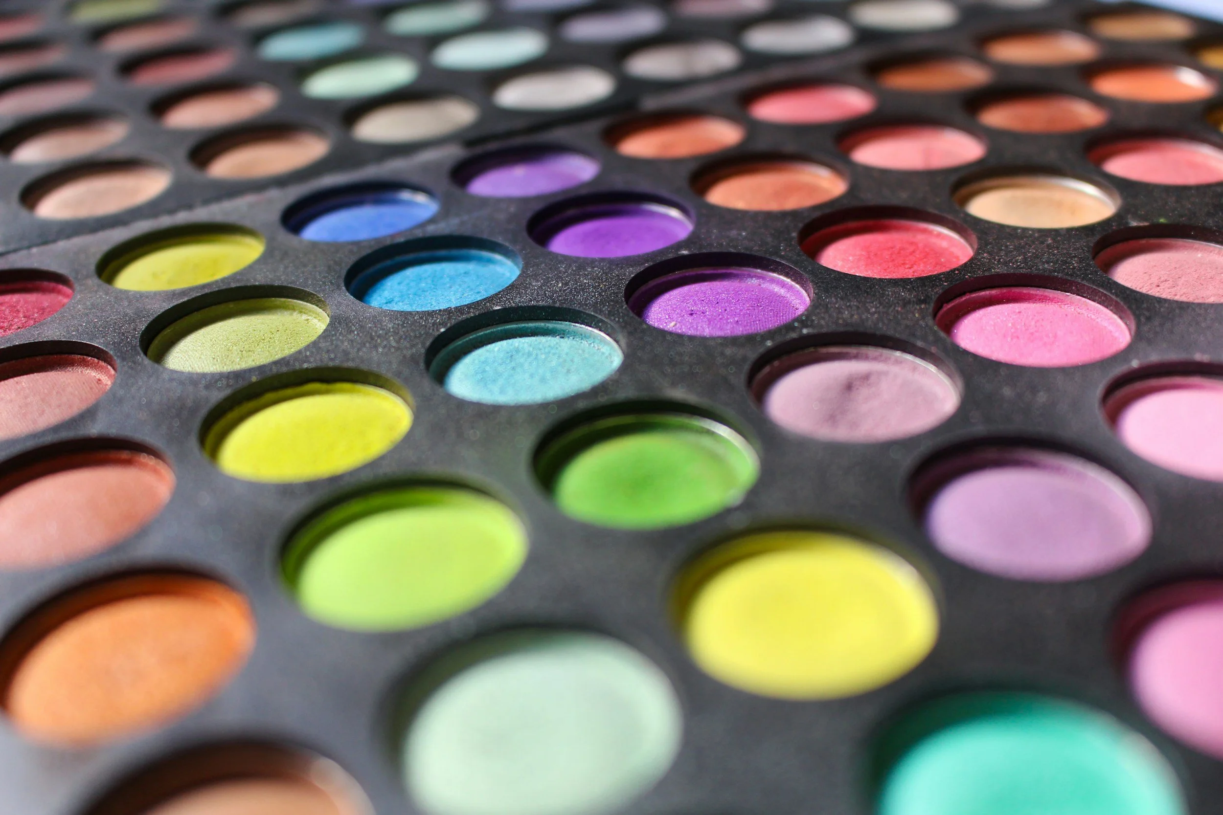 Close-up of a palette of round watercolor paints in a variety of colors including pink, purple, blue, green, yellow, and orange.