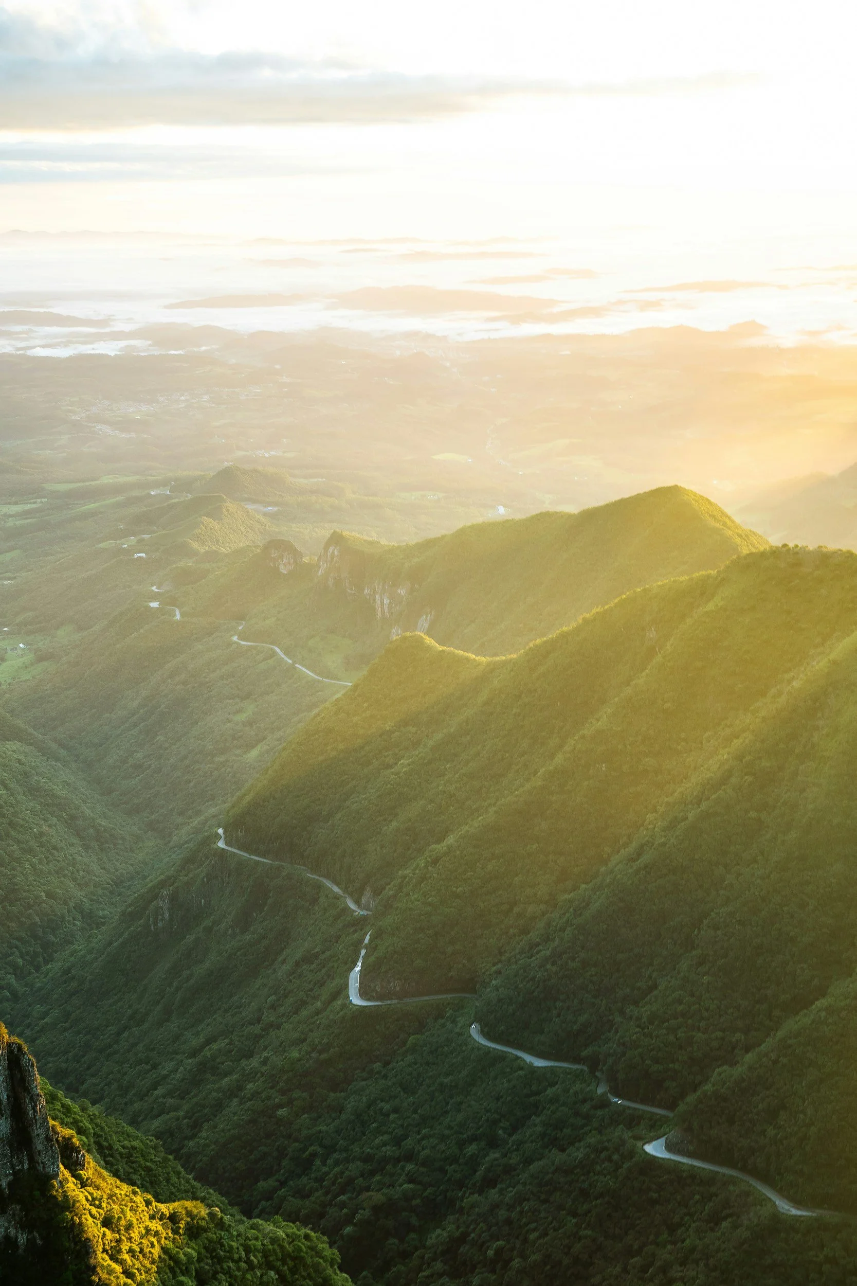 Sunlight illuminating green mountain ridges with a winding road through the valley below.