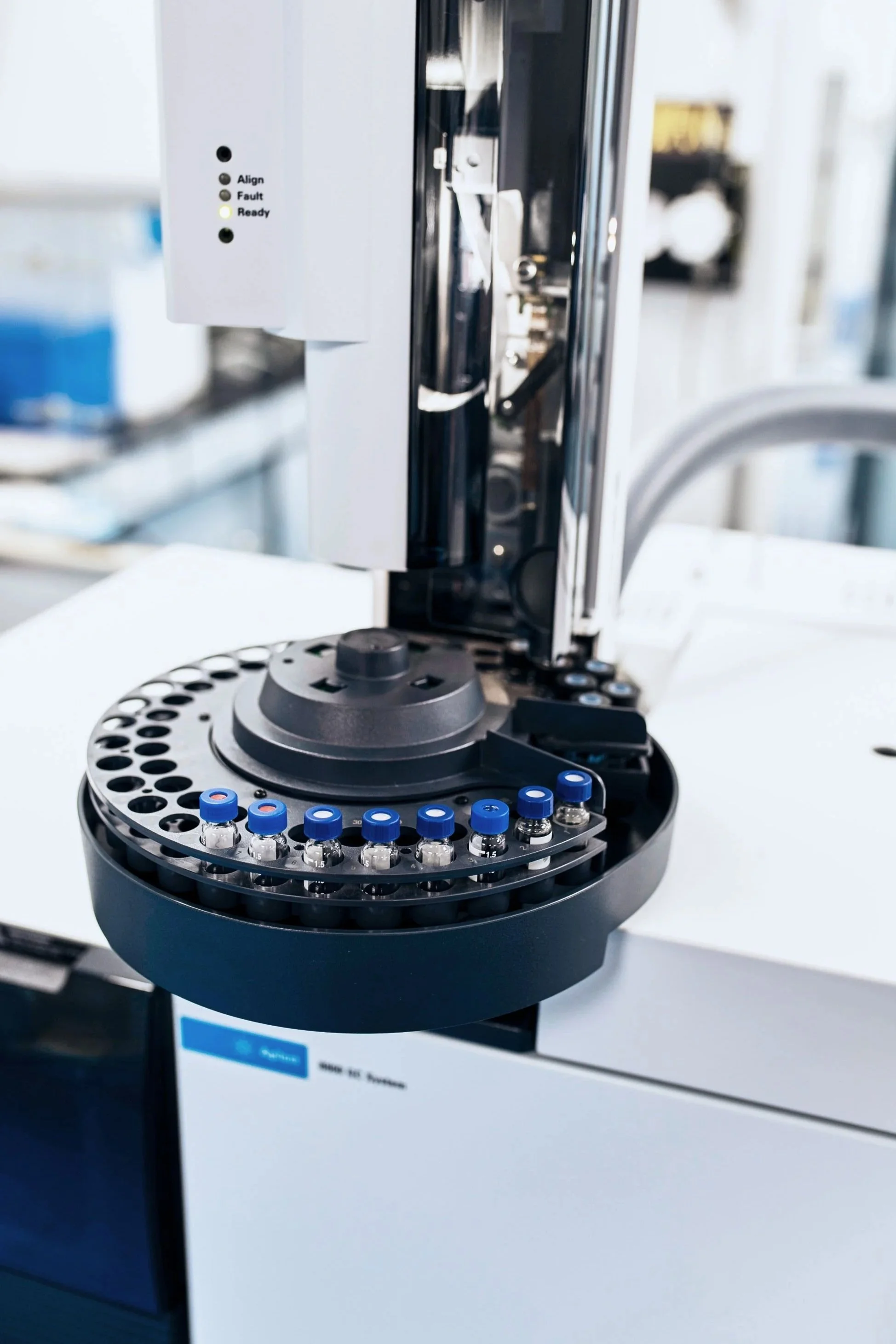 Laboratory instrument with a circular tray of small glass vials, some with blue caps, positioned within a scientific or medical setting.
