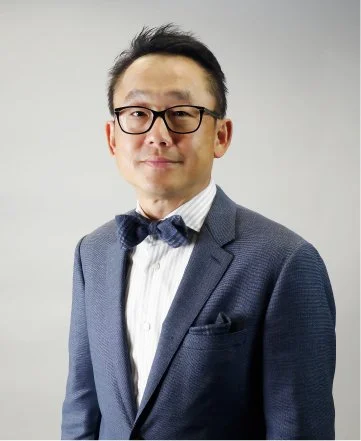 Portrait of a man in a suit and glasses with a neutral background.