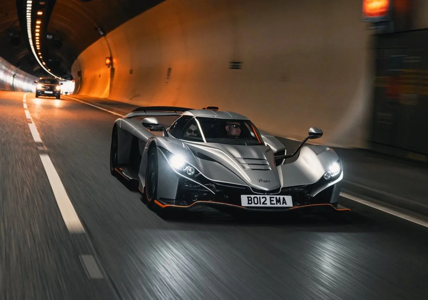 A silver Praga supercar driving through a tunnel at night.