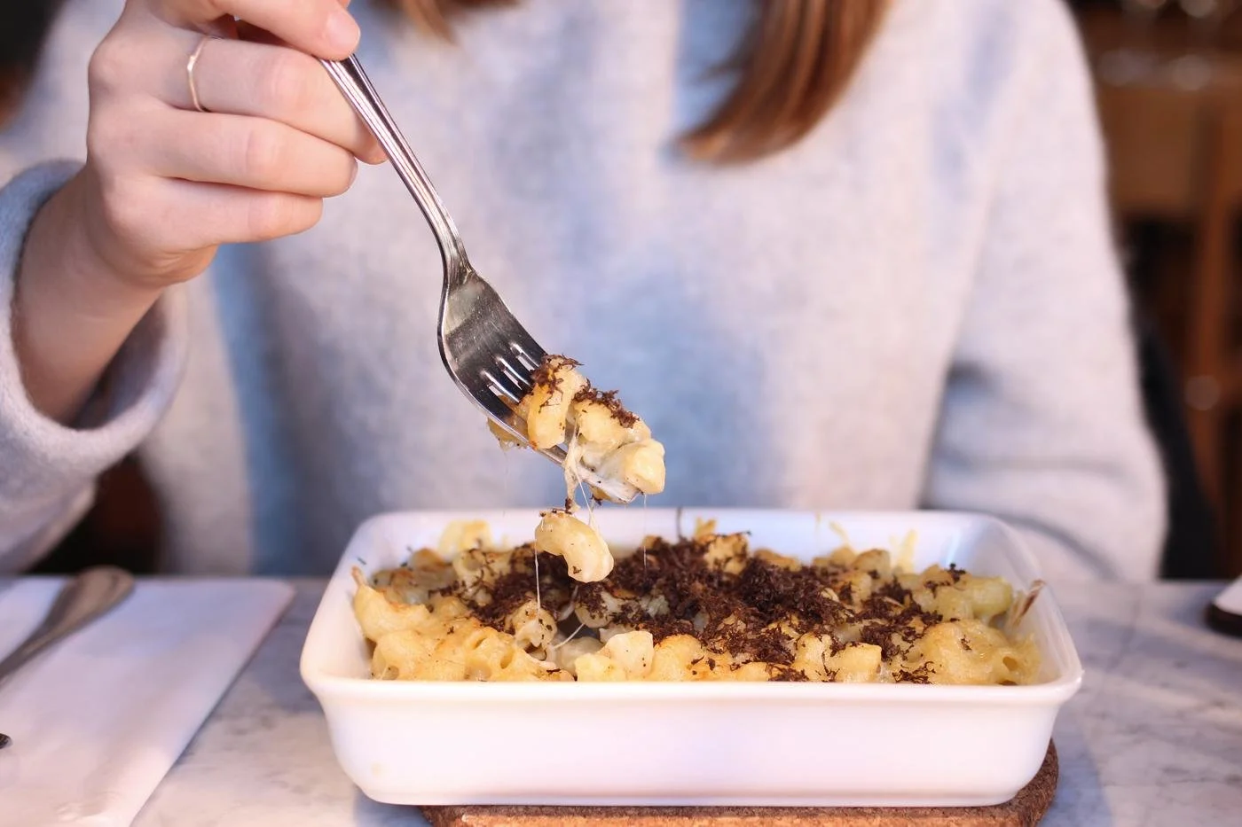 Person mangeant des pâtes gratinées avec du fromage râpé et du poivre dans un restaurant.
