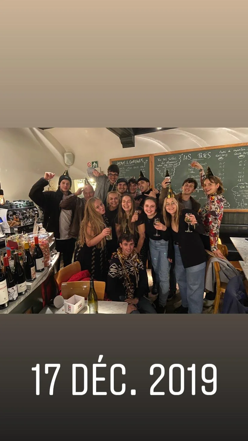 Groupe de jeunes amis célébrant lors d'une fête de Noël ou de fin d'année, certains portant des accessoires festifs, dans un café ou un bar, avec des bouteilles de vin sur la table, le 17 décembre 2019.