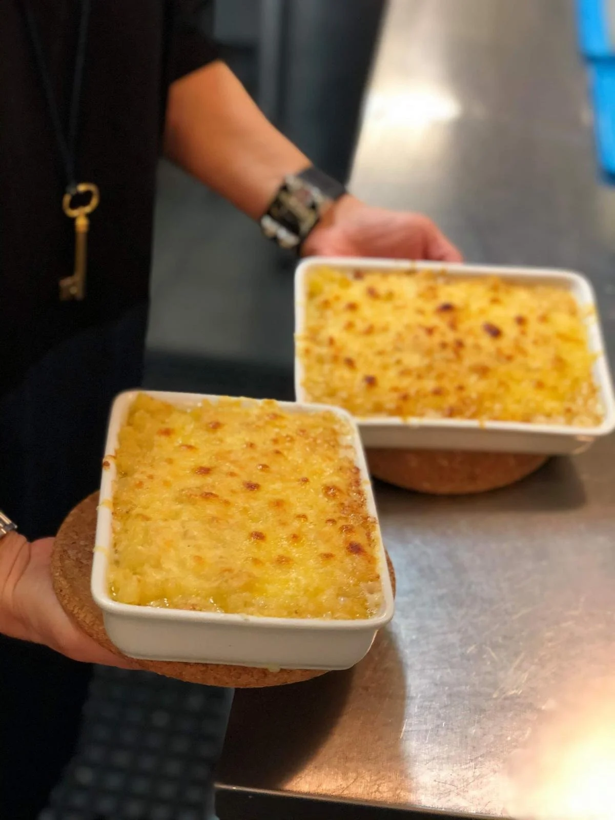 Deux mains tenant des plats de gratin de pommes de terre, posés sur des dessous de verre en forme de rond, dans une cuisine