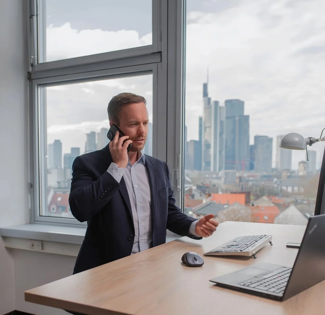 Geschäftsmann in Anzug spricht am Telefon in einem Büro mit Blick auf die Skyline einer Stadt