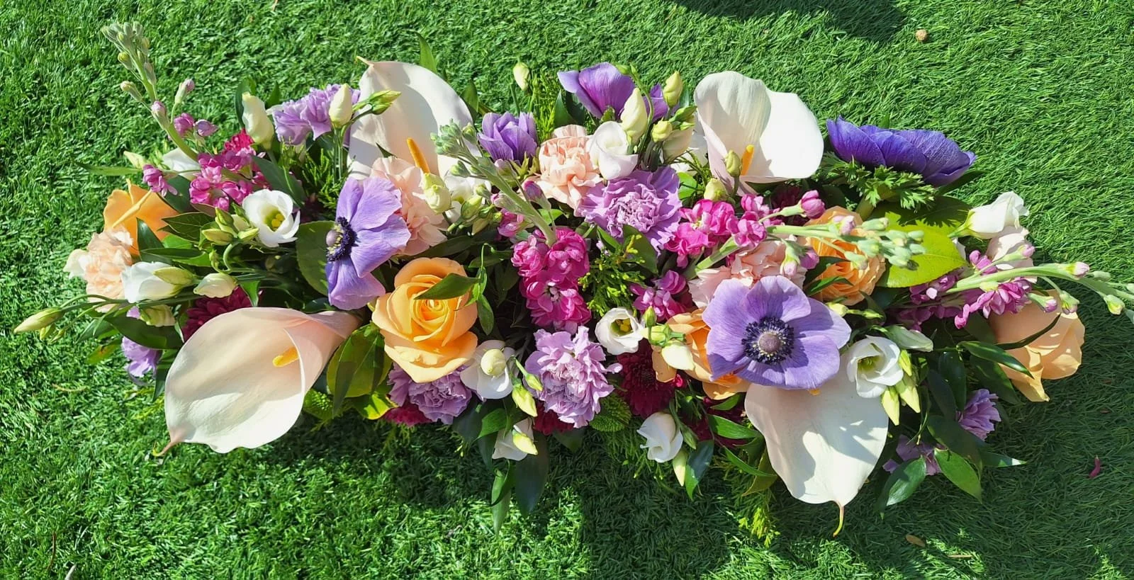 White, orange and purple flowers are arranged together on a carpet of bright green grass