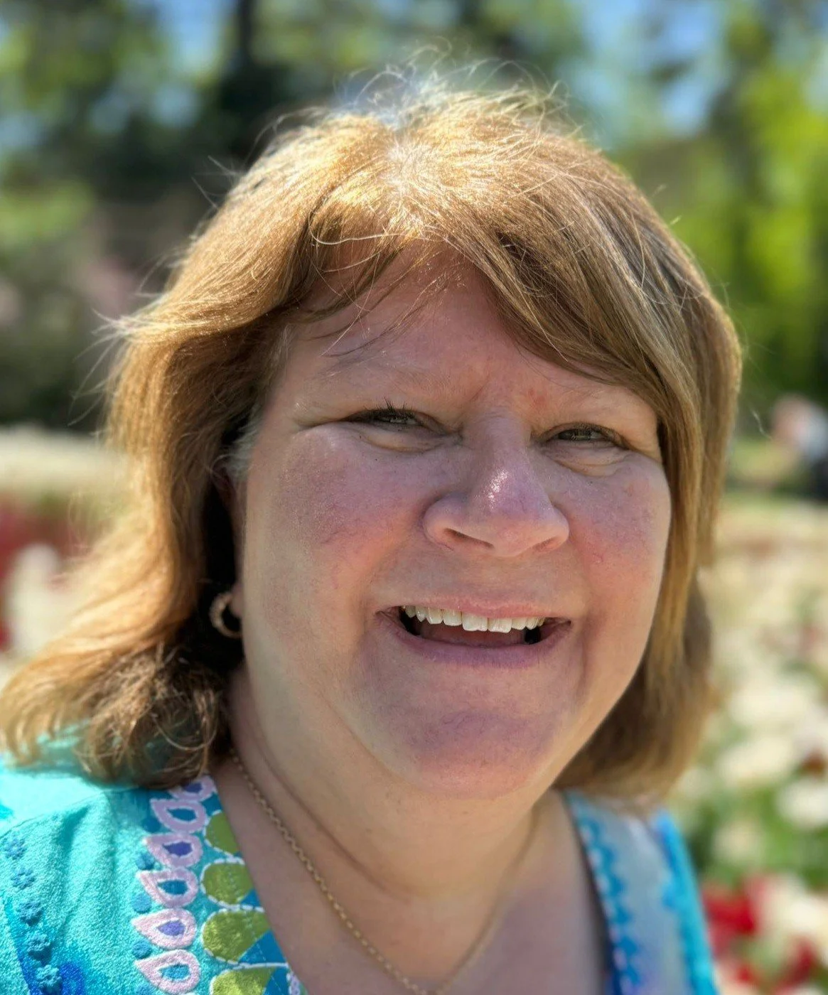 A white woman in her fifties with warm blonde hair is wearing a blue an turquoise top. She smiles so broadly at the camera that her eyes almost disappear. She wears gold earings with a matching necklace. This is Cathy Giplin, counsellor.