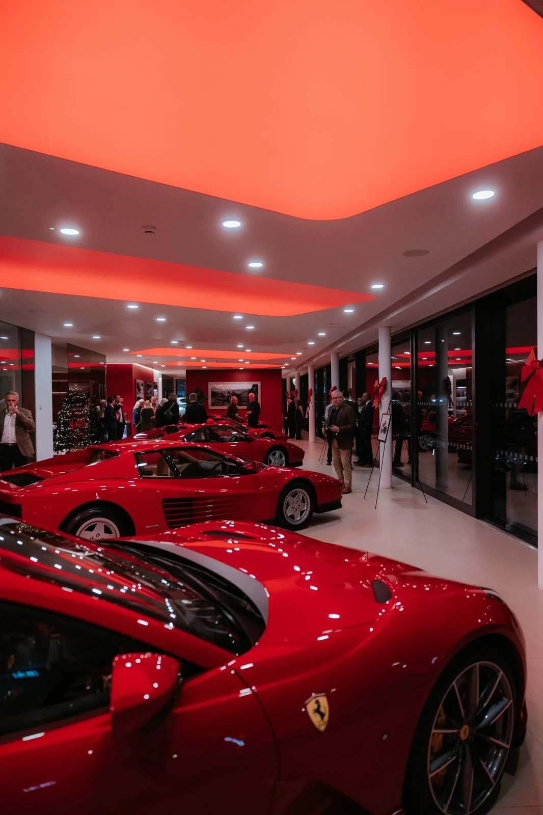 Red Ferrari sports cars with people viewing them inside a showroom decorated for Christmas.