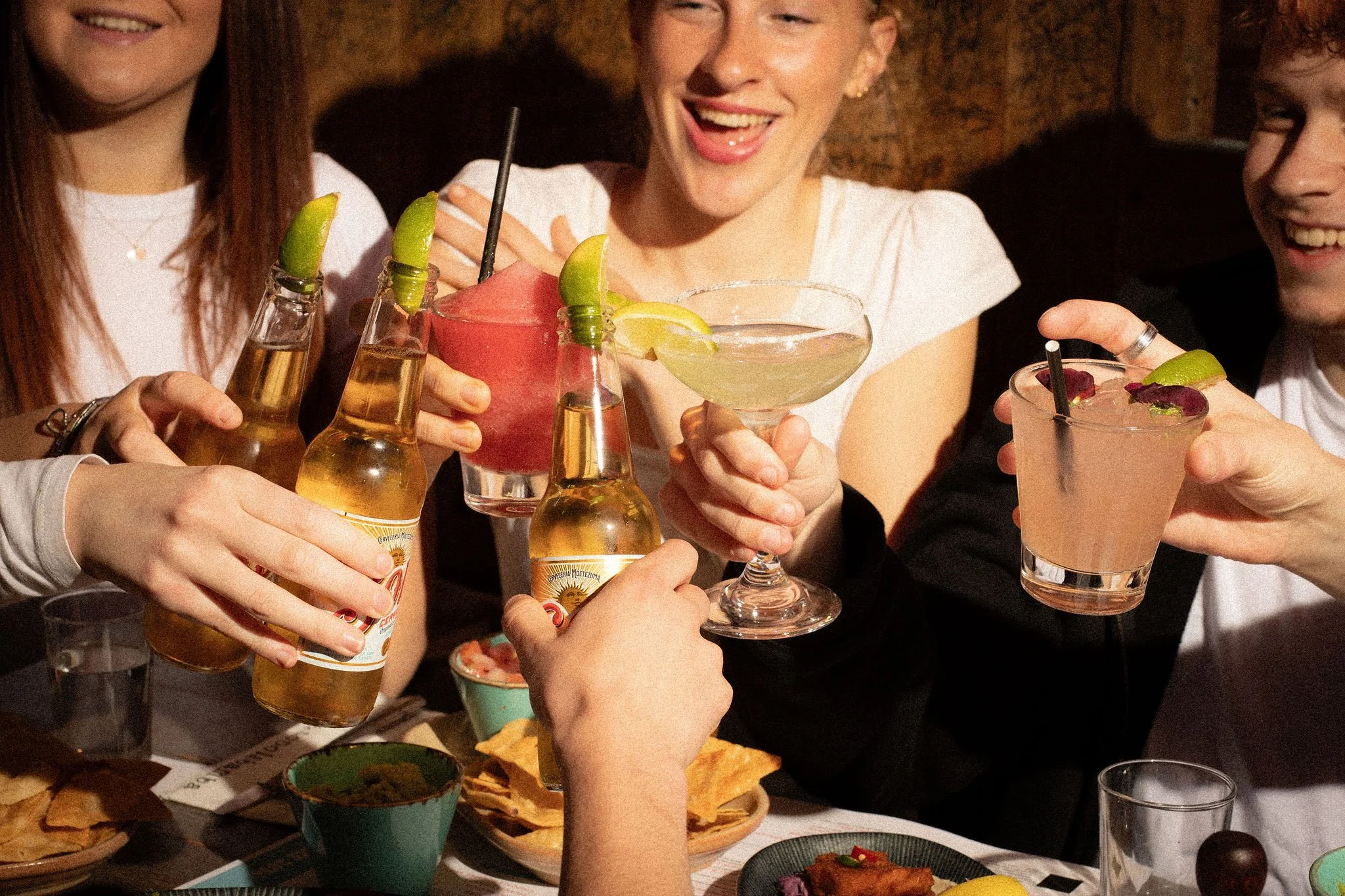People enjoying drinks at a social gathering, with various cocktails and beer bottles on the table.