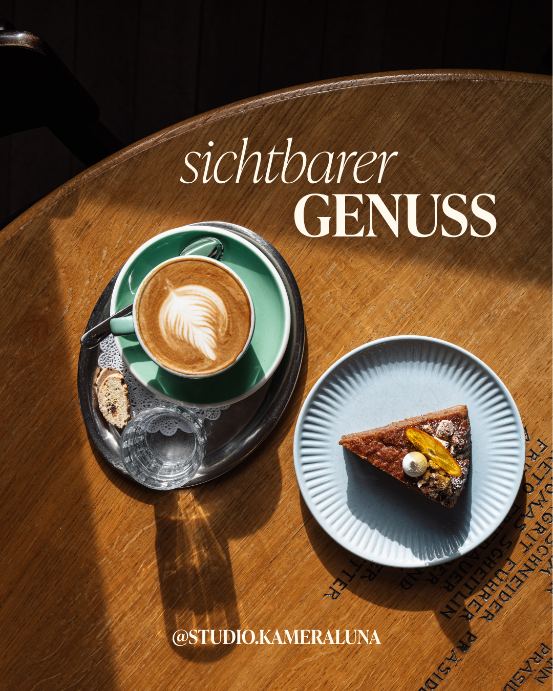 Ein grüner Kaffee mit Latte-Art auf einem silbernen Tablett, daneben eine weiße Schale mit einem Stück Schokoladentorte auf einem Holztablett.