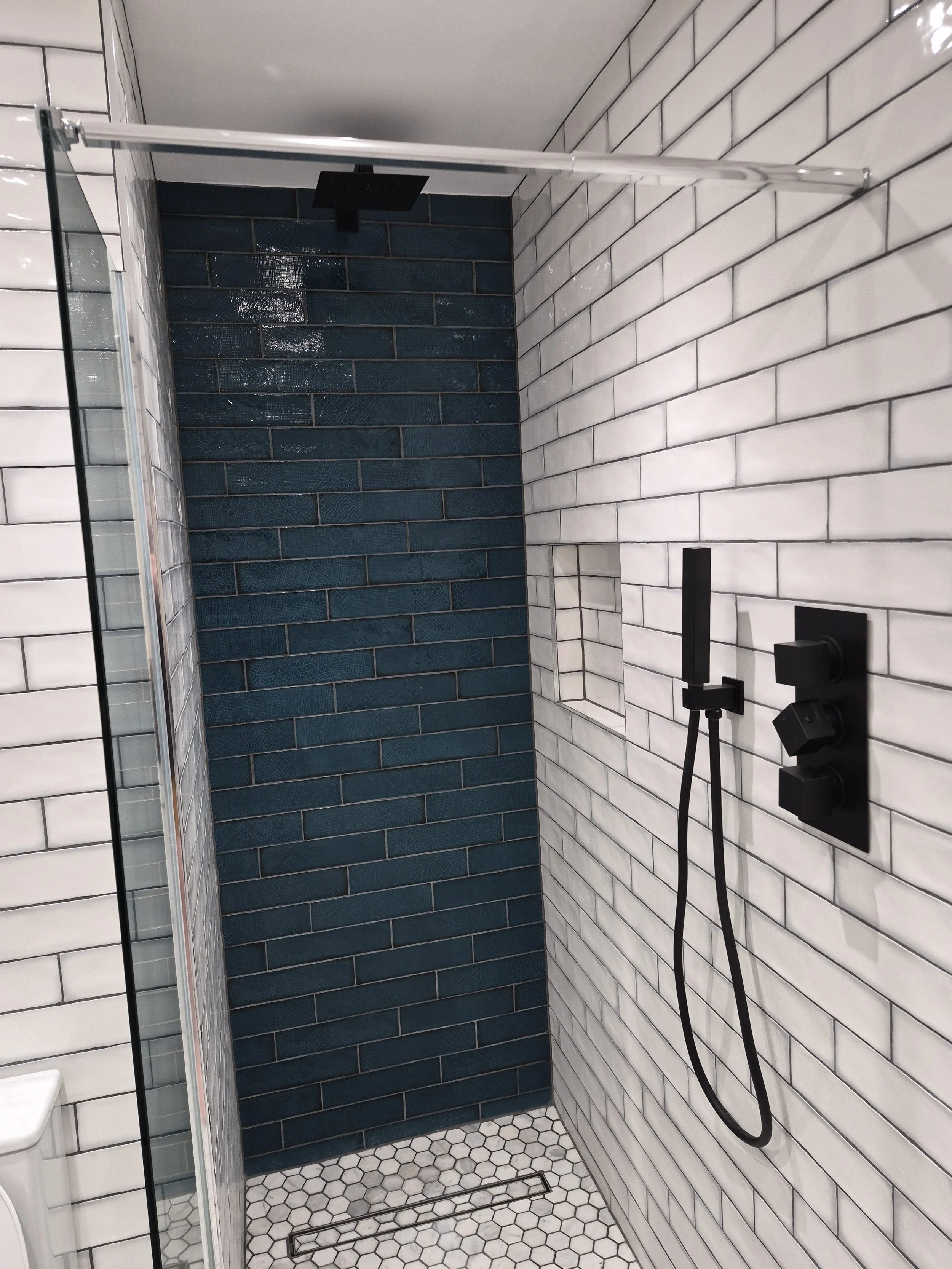 Modern shower with black rainfall showerhead, black handheld shower, and white subway tile walls, one wall accented with dark blue tiles.