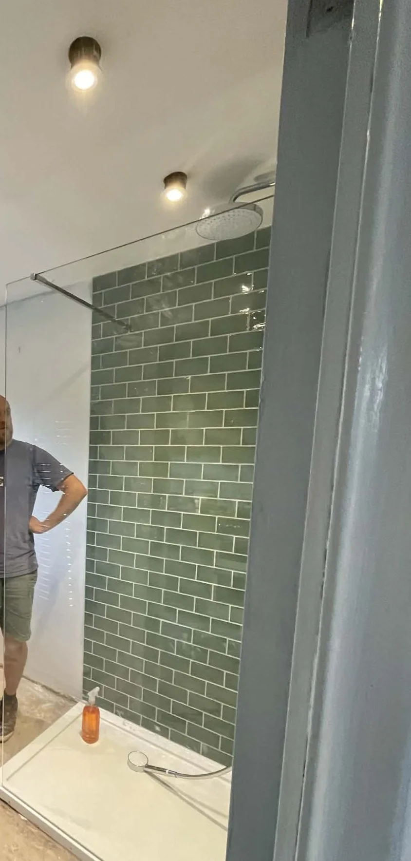 A modern walk-in shower with green subway tiles, a rain shower head, and a glass shower door.