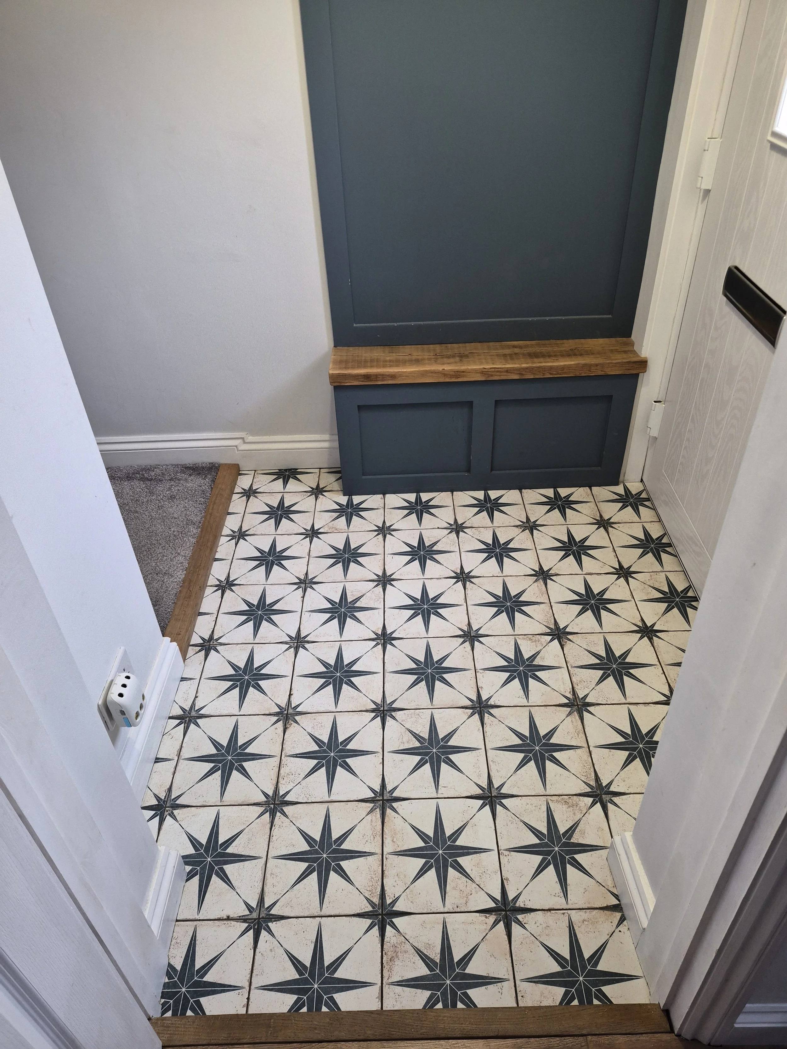 Tile floor with a black and white geometric star pattern, blue wall with a wooden trim, and a white door with a black mailbox slot.