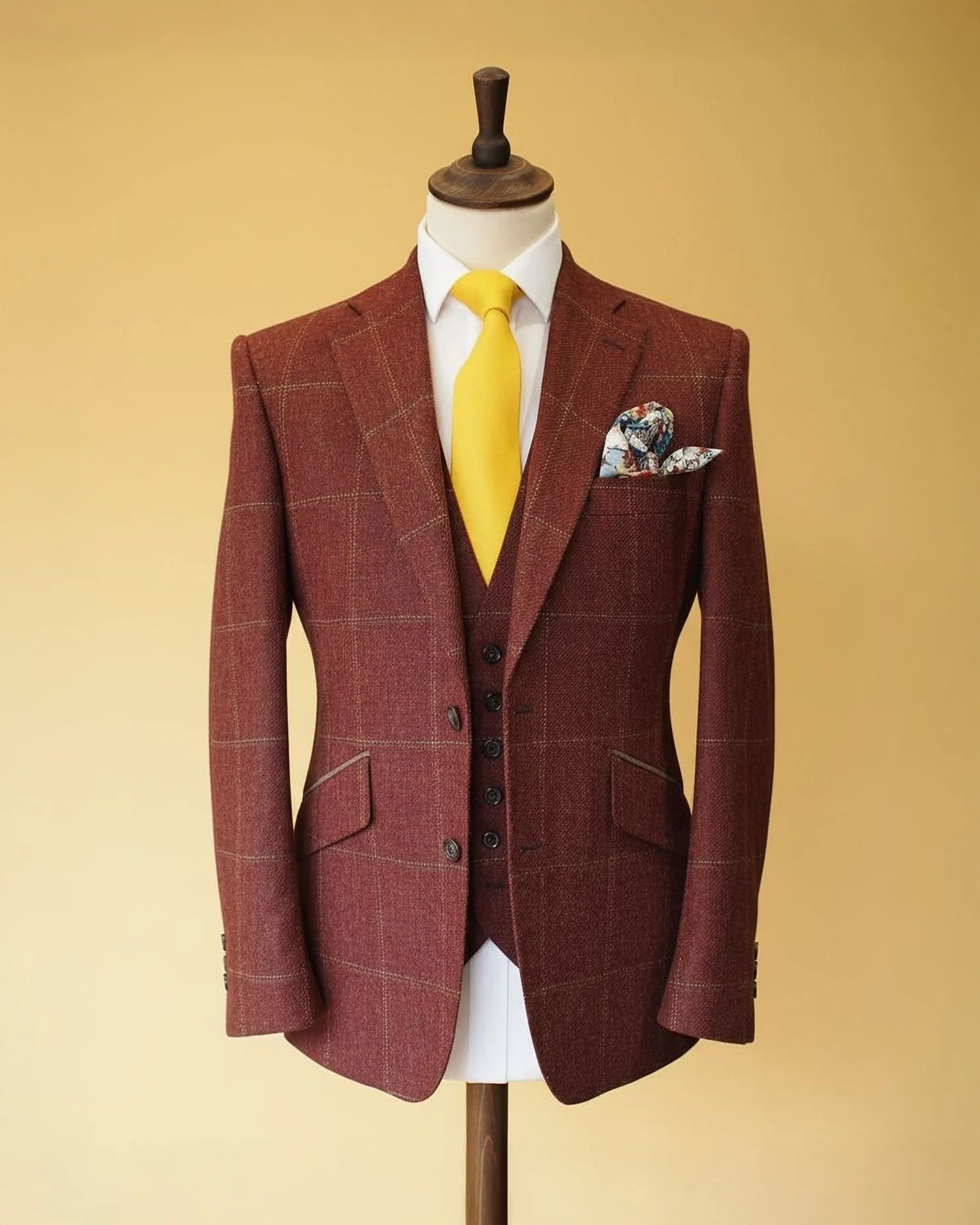 A mannequin wearing a red plaid blazer with a white shirt, yellow tie, and a colorful pocket square, set against a beige background.