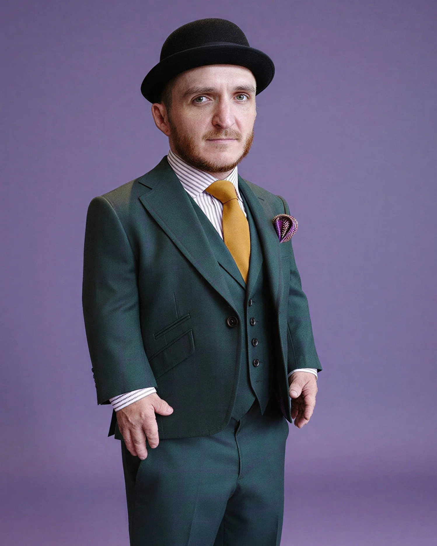 Man wearing a dark green suit, white striped shirt, yellow tie, and black bowler hat, against a purple background.