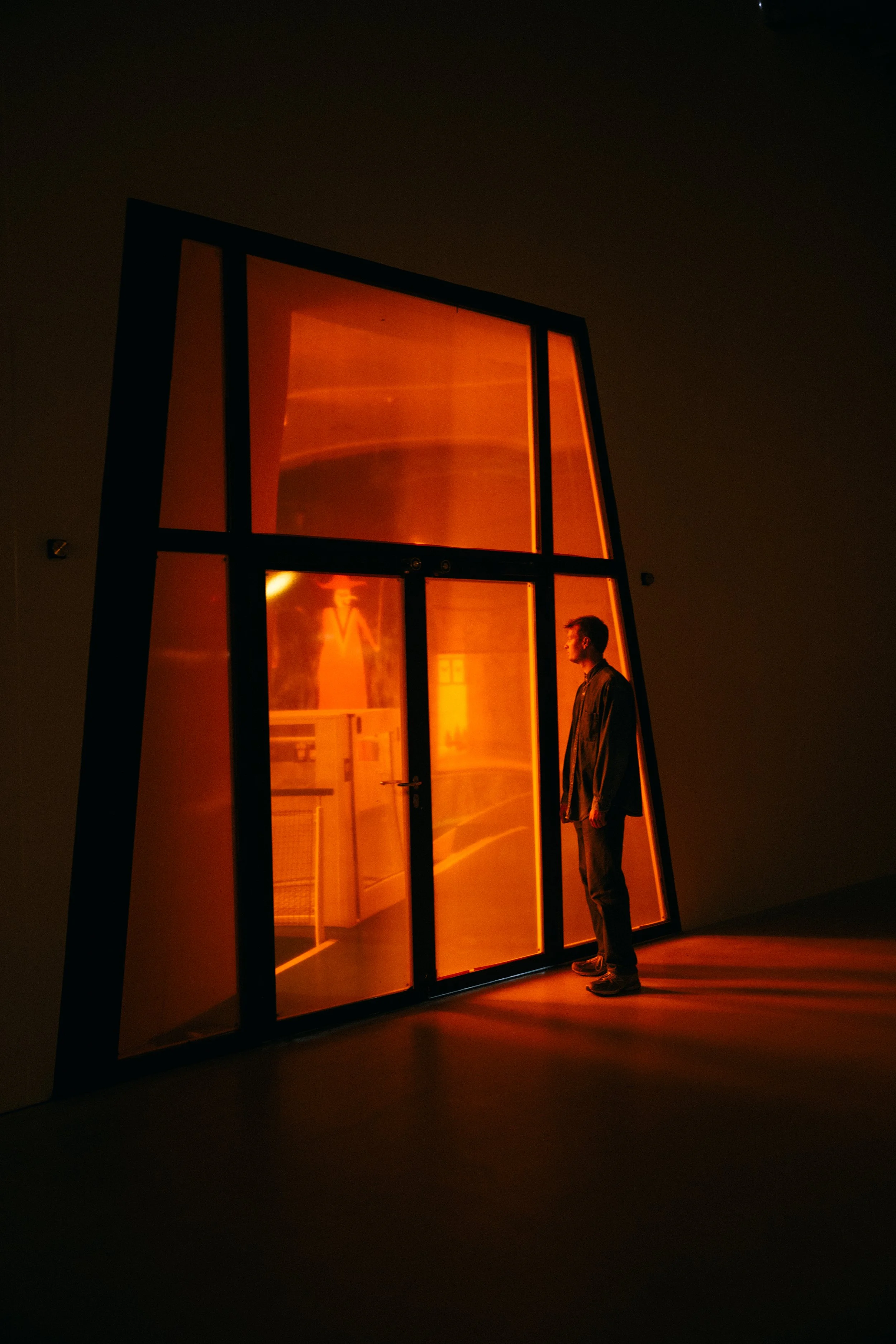 A man standing in front of a large illuminated orange display or installation with a black metal frame, inside a dark room.