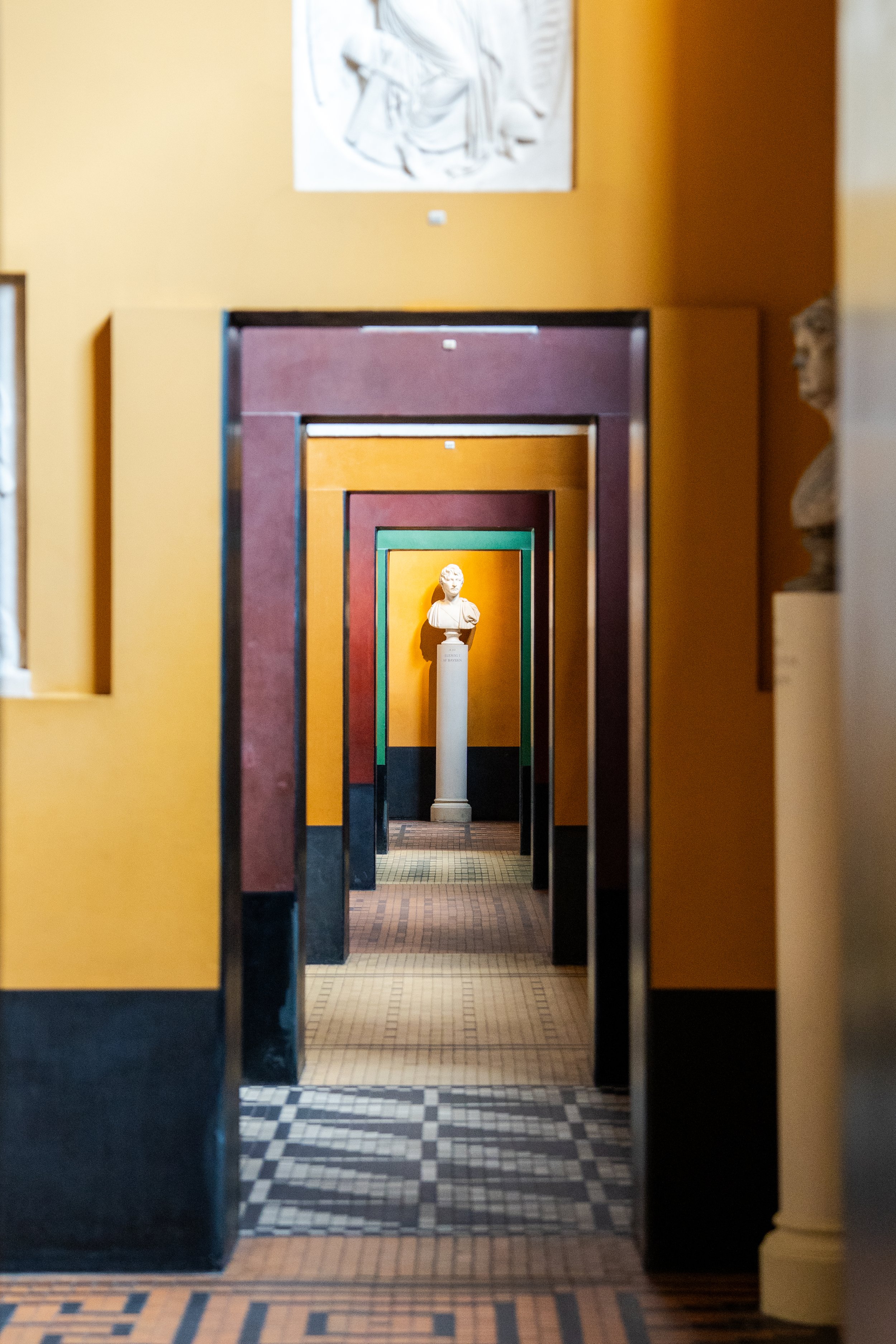 Multiple doorways in varying colors, creating a tunnel effect with a sculpture of a bust at the far end.