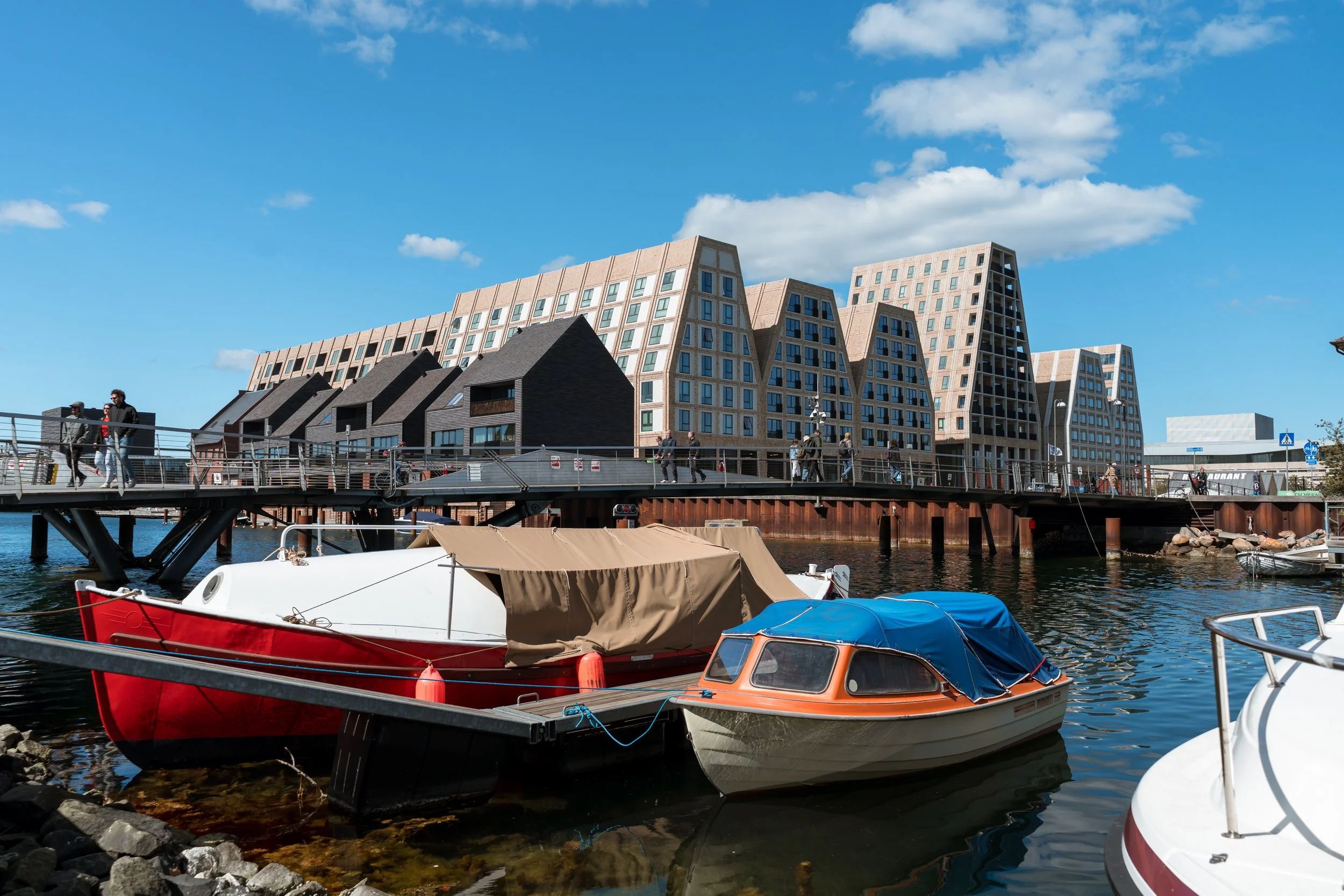 Boats docked at a harbor with modern buildings in the background under a clear blue sky.