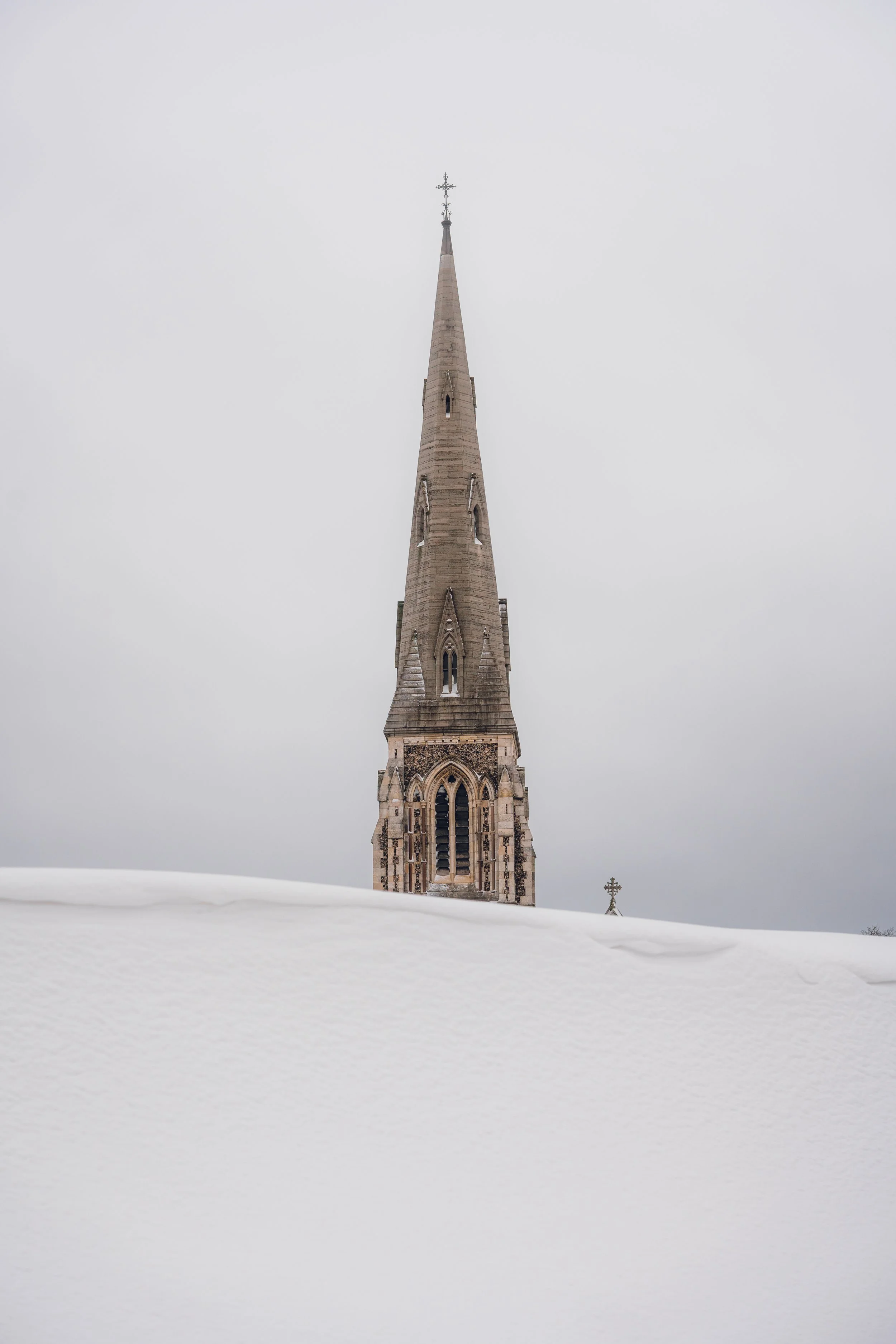 A church steeple rising above a snow-covered landscape on a cloudy day.