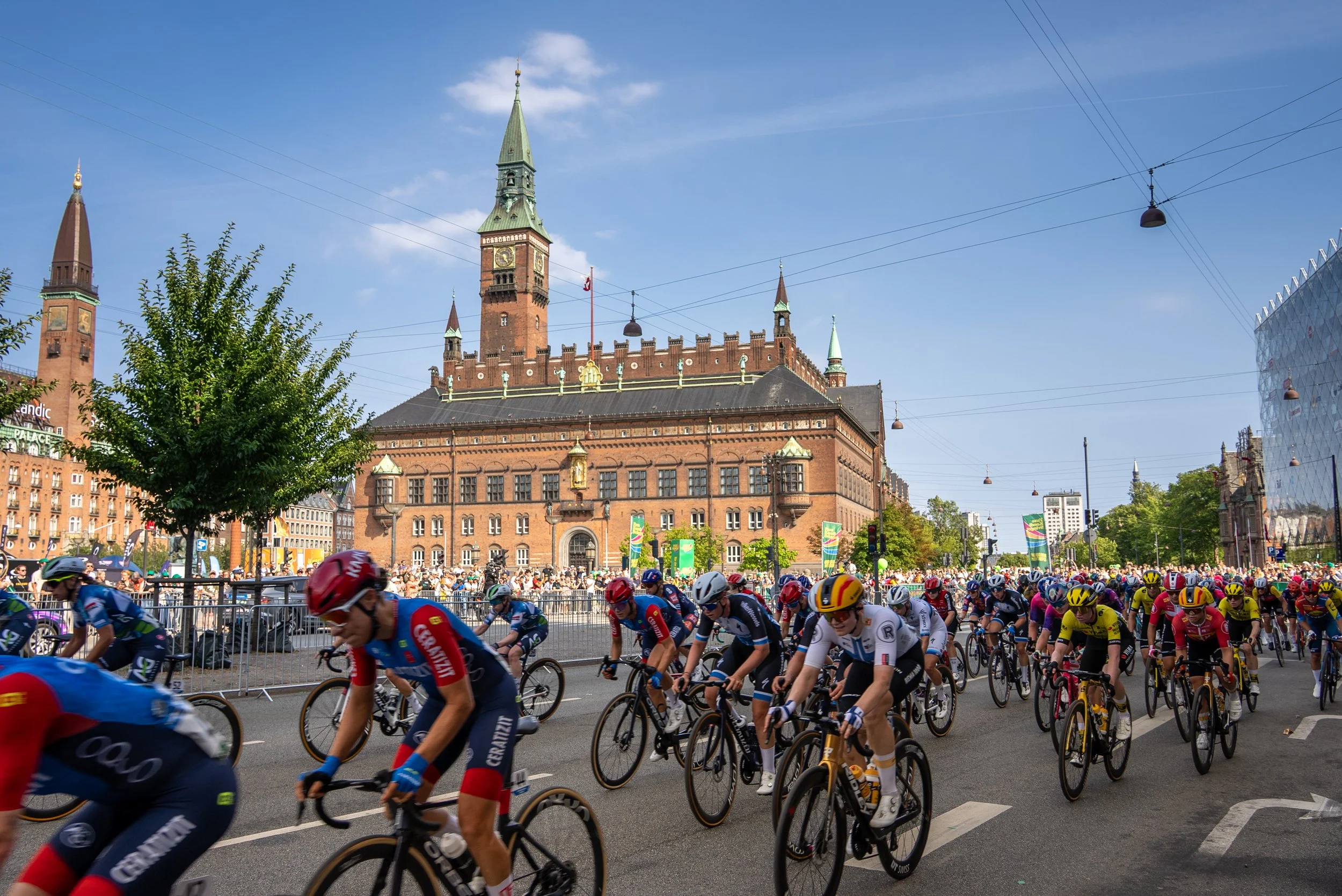 Cyclists participating in a race or event in front of a historic building with towers and a clock in a city square,