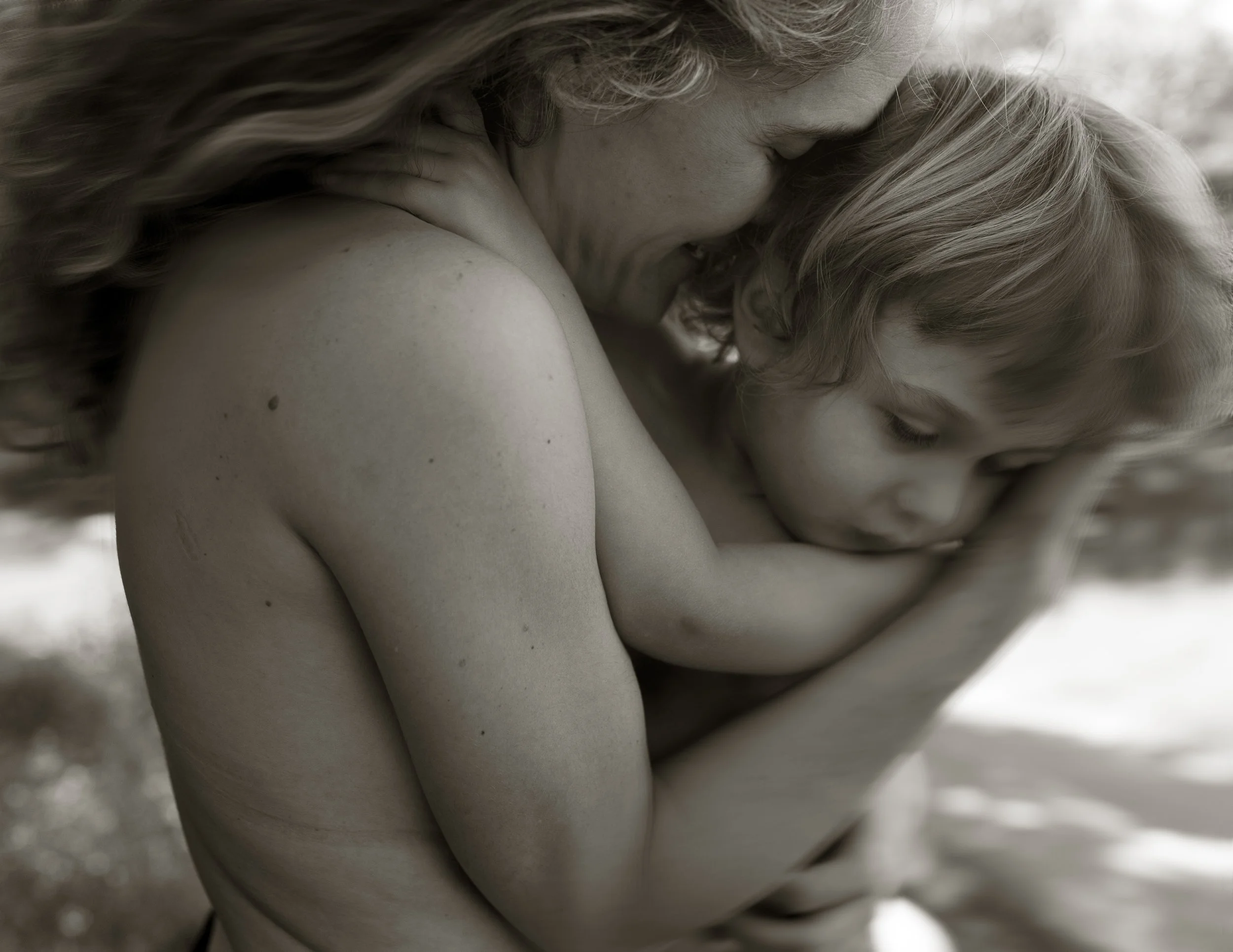 Two women with curly and wavy hair embracing closely, with one resting her head on the other's shoulder.