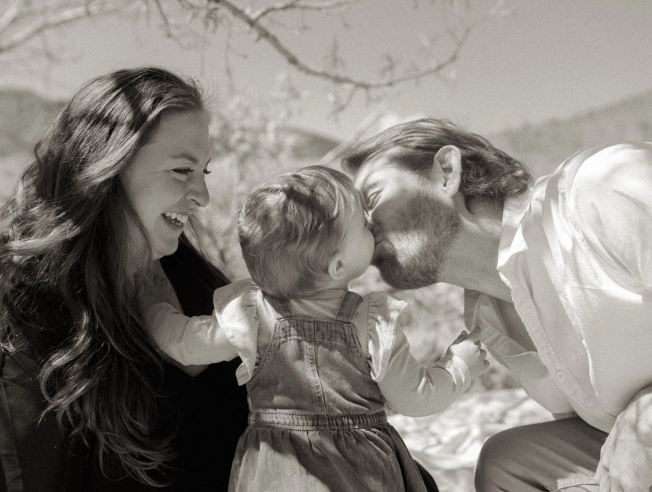 A black and white photo of a family with two women and two children, smiling and looking at each other outdoors.