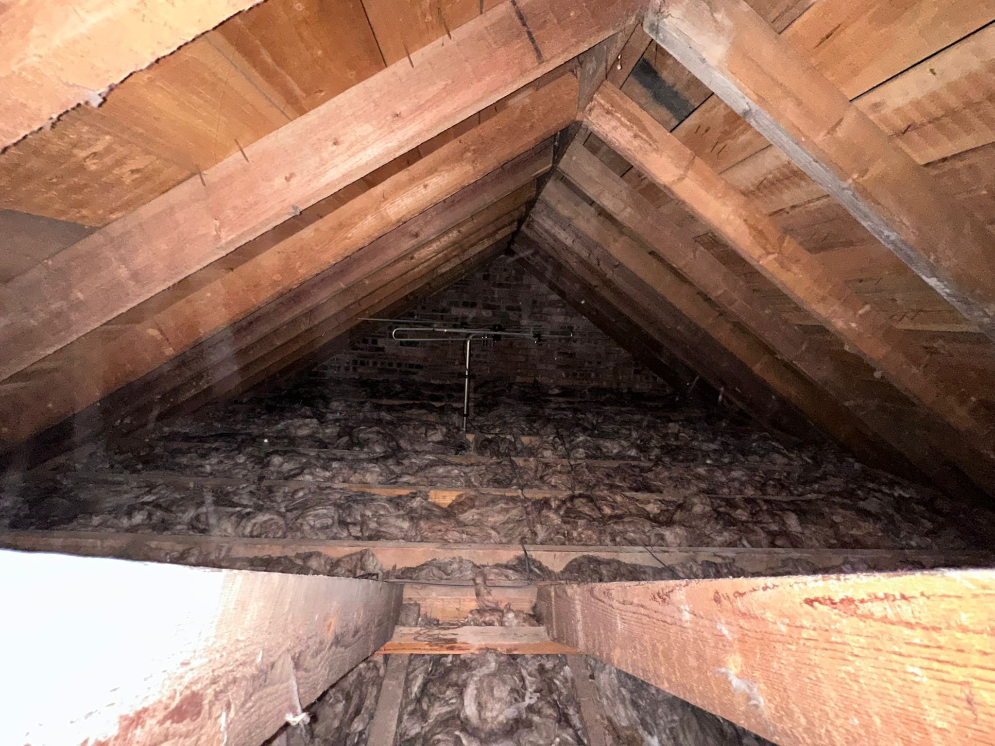 Inside view of an attic with exposed wooden beams and a dark, textured floor beneath.