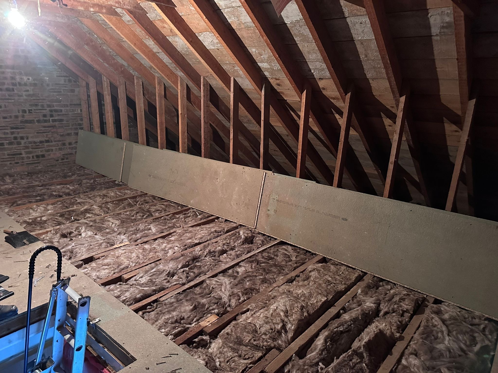 Attic or unfinished room with exposed wooden beams and insulation material on the floor, with some drywall or wall panel leaning against the structure.