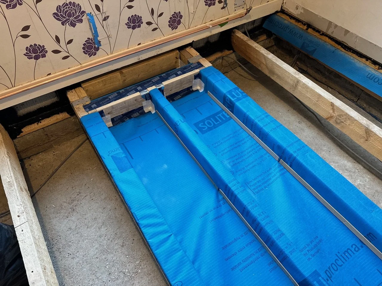 Bathroom floor renovation showing blue waterproofing membrane installed between wooden floor joists.