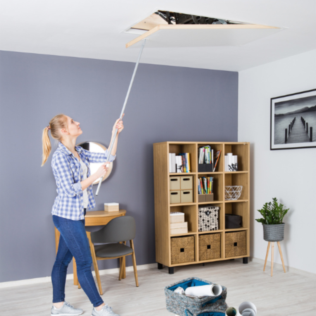 A woman painting a ceiling with a roller in a room with modern decor and a bookshelf.