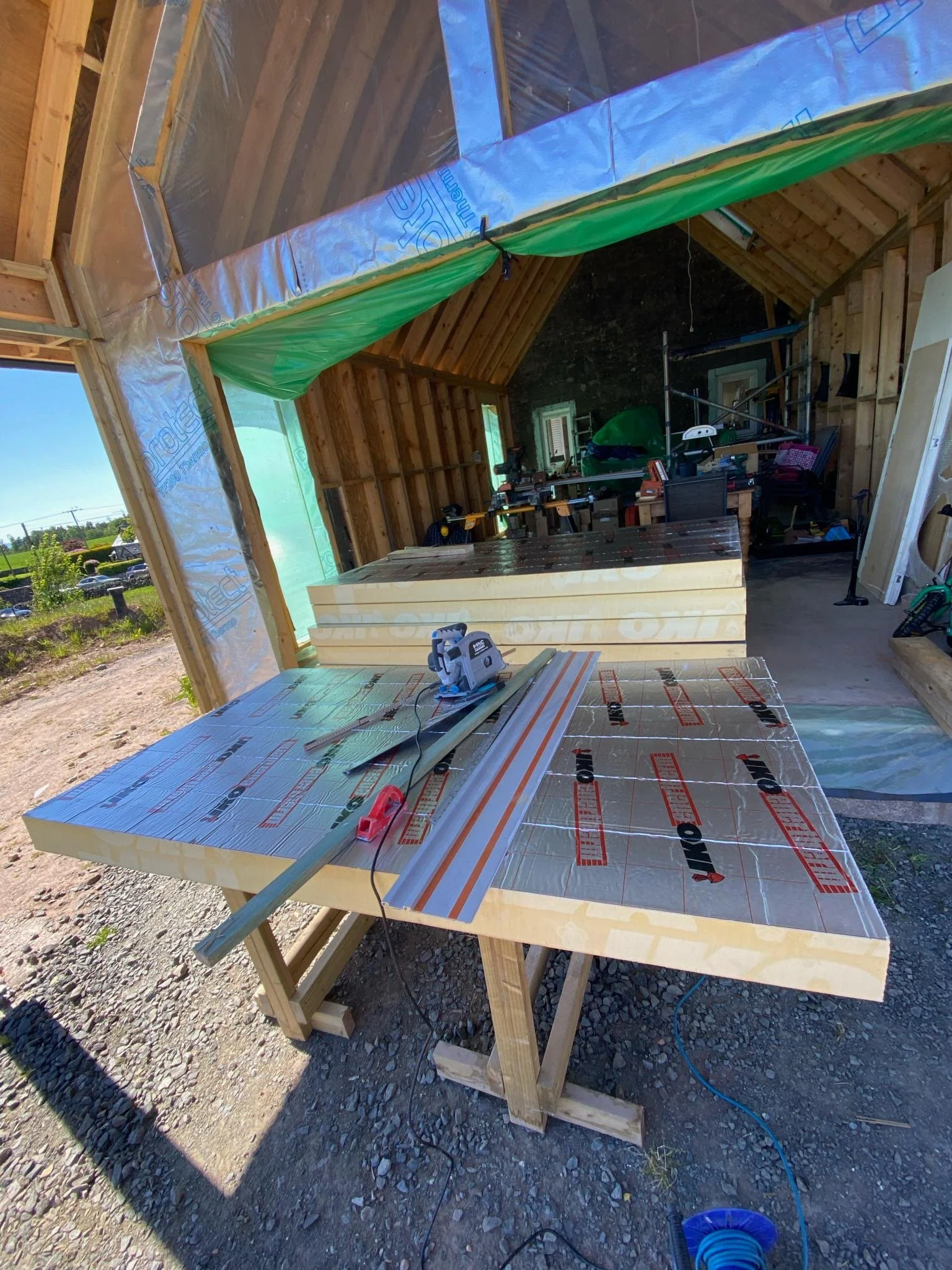 Construction site inside a partially built wooden house, with insulation and construction tools on workbenches and a gravel floor.