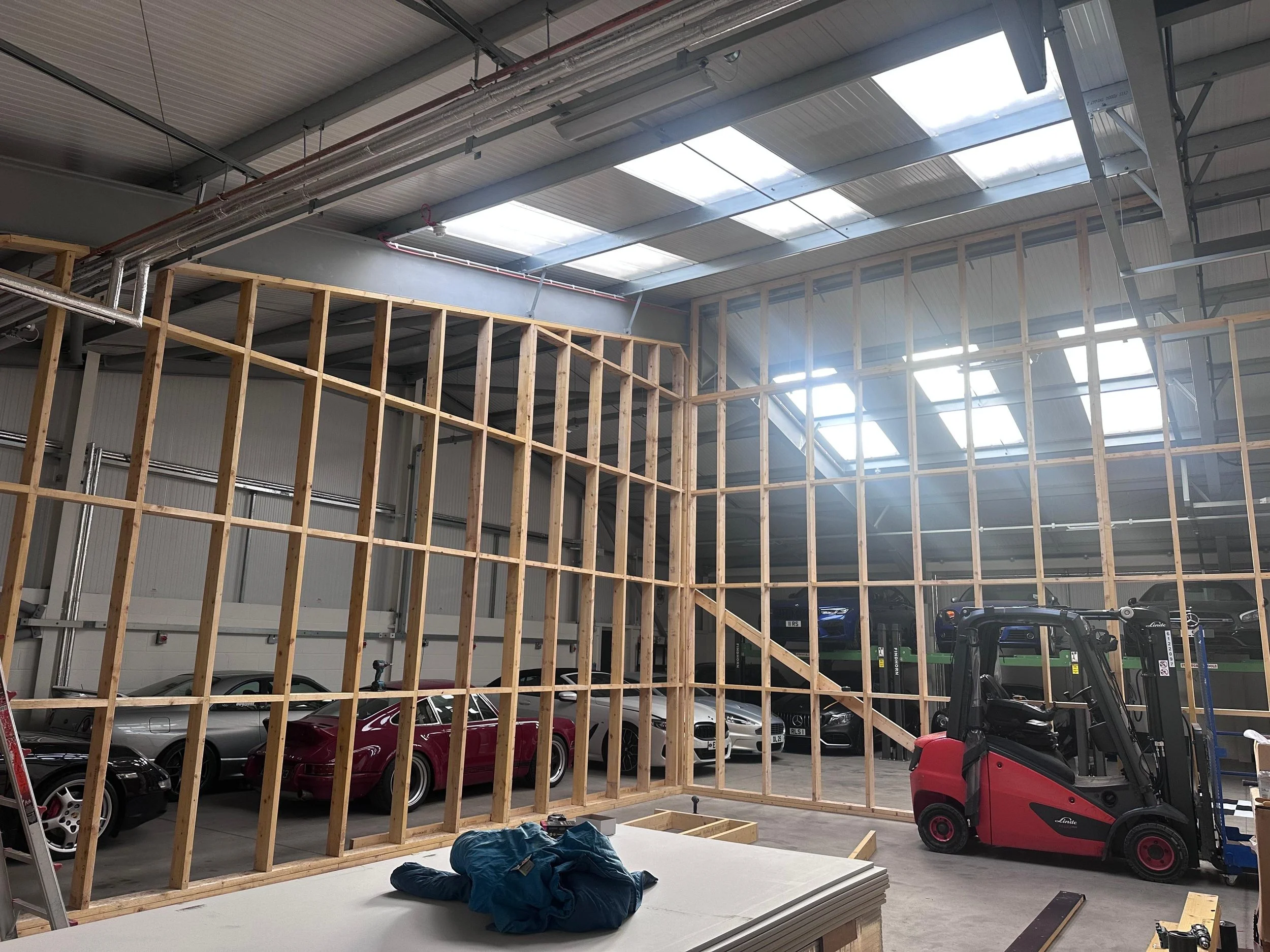 Interior view of a warehouse or garage under construction with wooden framing, parked cars, and a forklift.