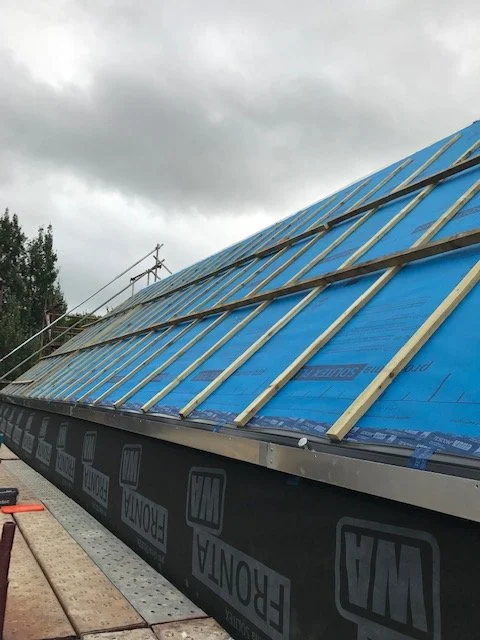 Roof under construction with blue weatherproofing material and wooden battens installed.