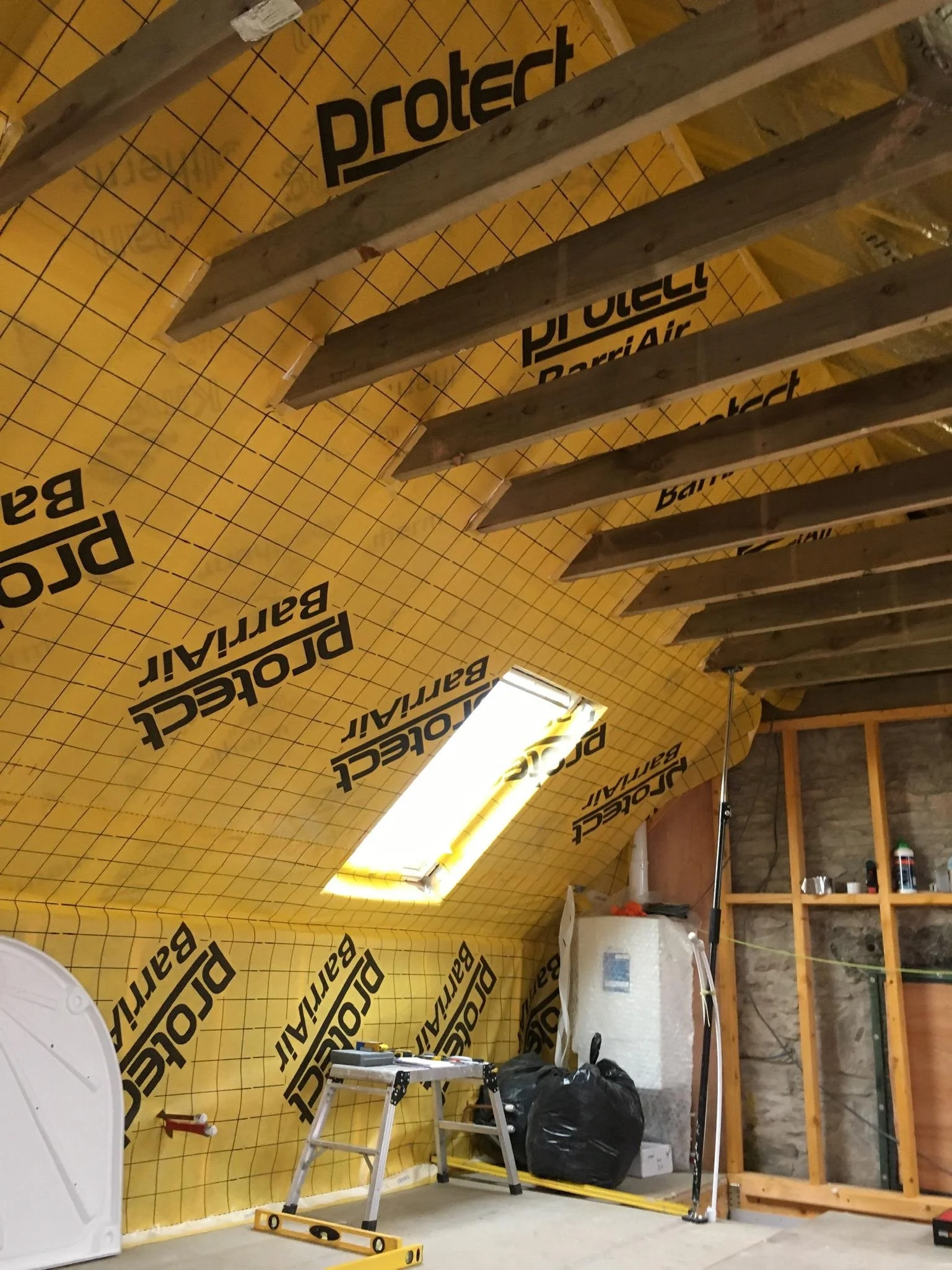 Insulation boards on the ceiling with wooden beams, a small step ladder, construction tools, and a work area under renovation.
